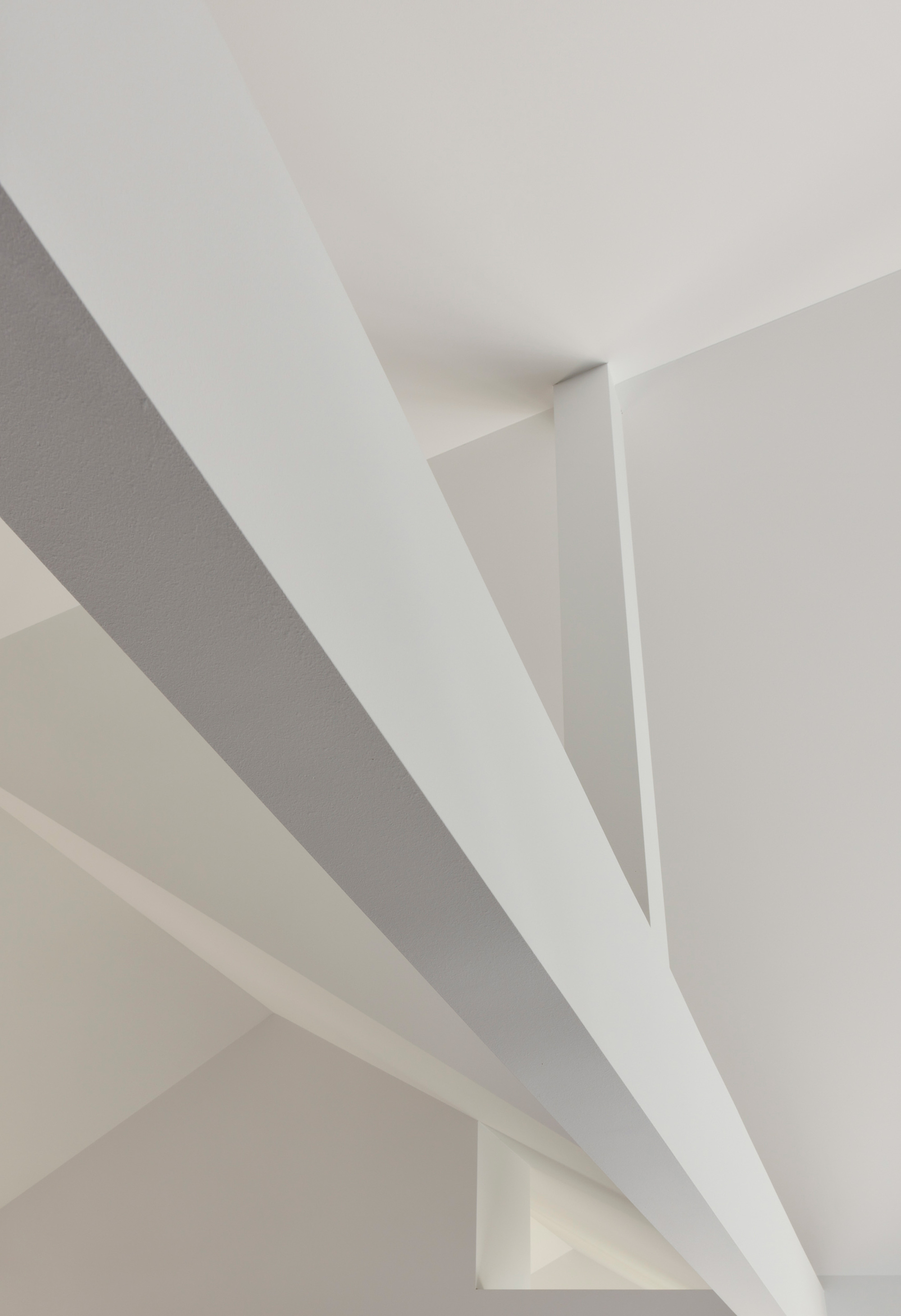 Ceiling detail showing white painted steel beams crossing at angles in soft daylight