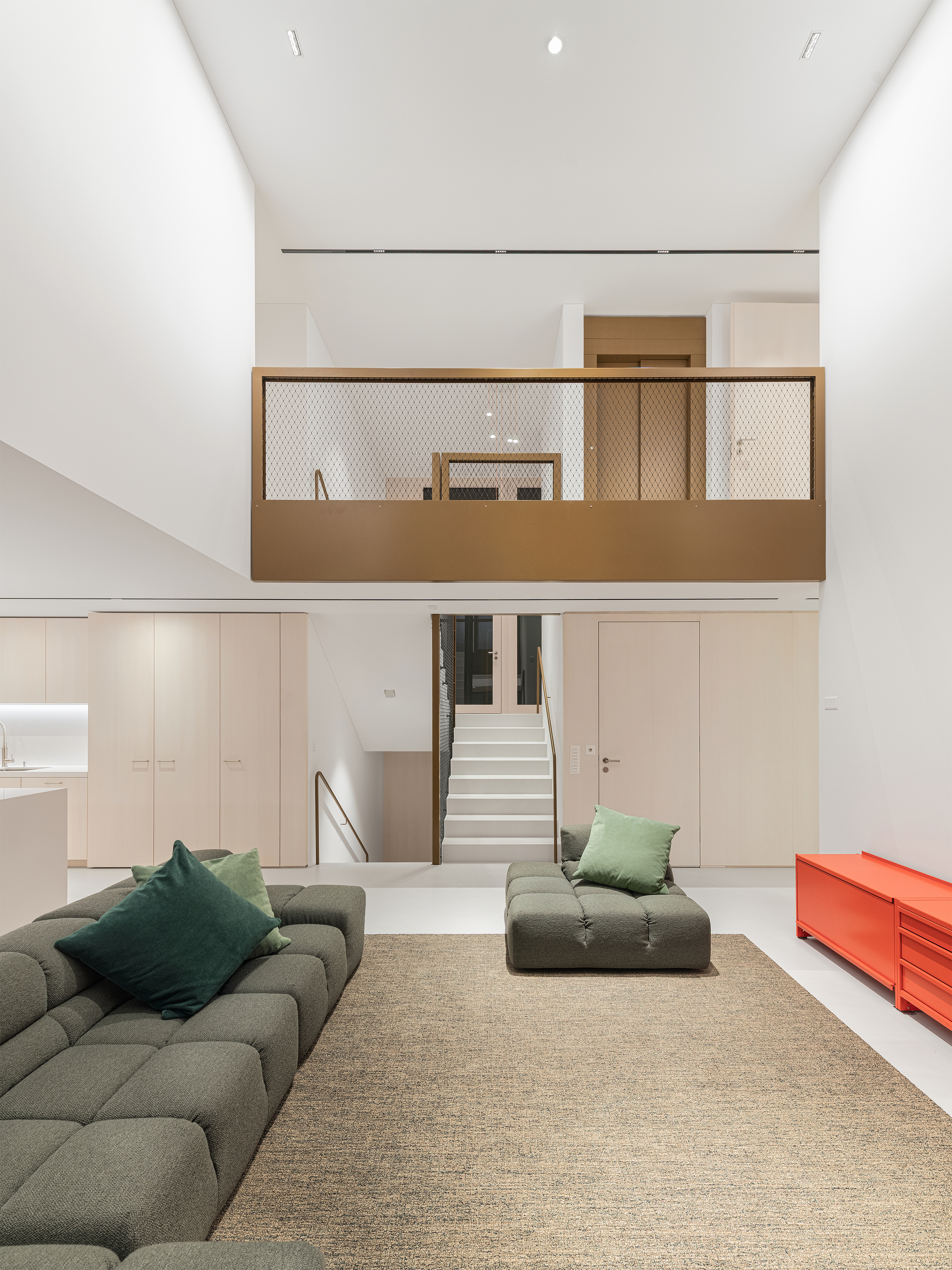 Double-height living room with suspended timber and mesh balcony above built-in storage and stair