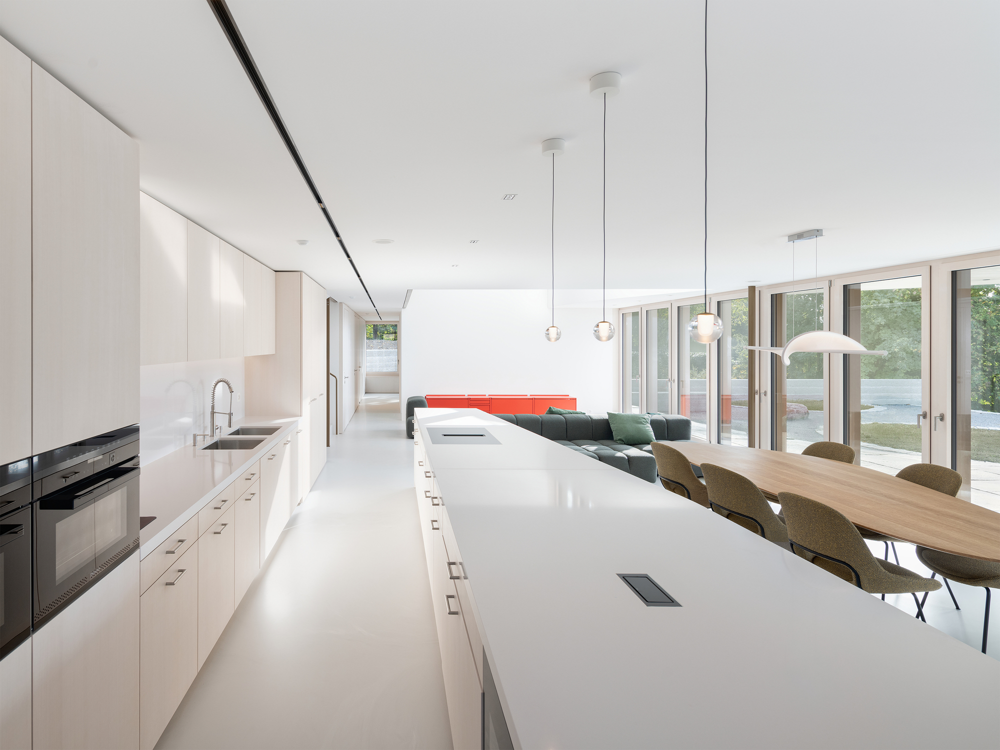 Open kitchen with white island and pendant lights extending into dining area with garden doors