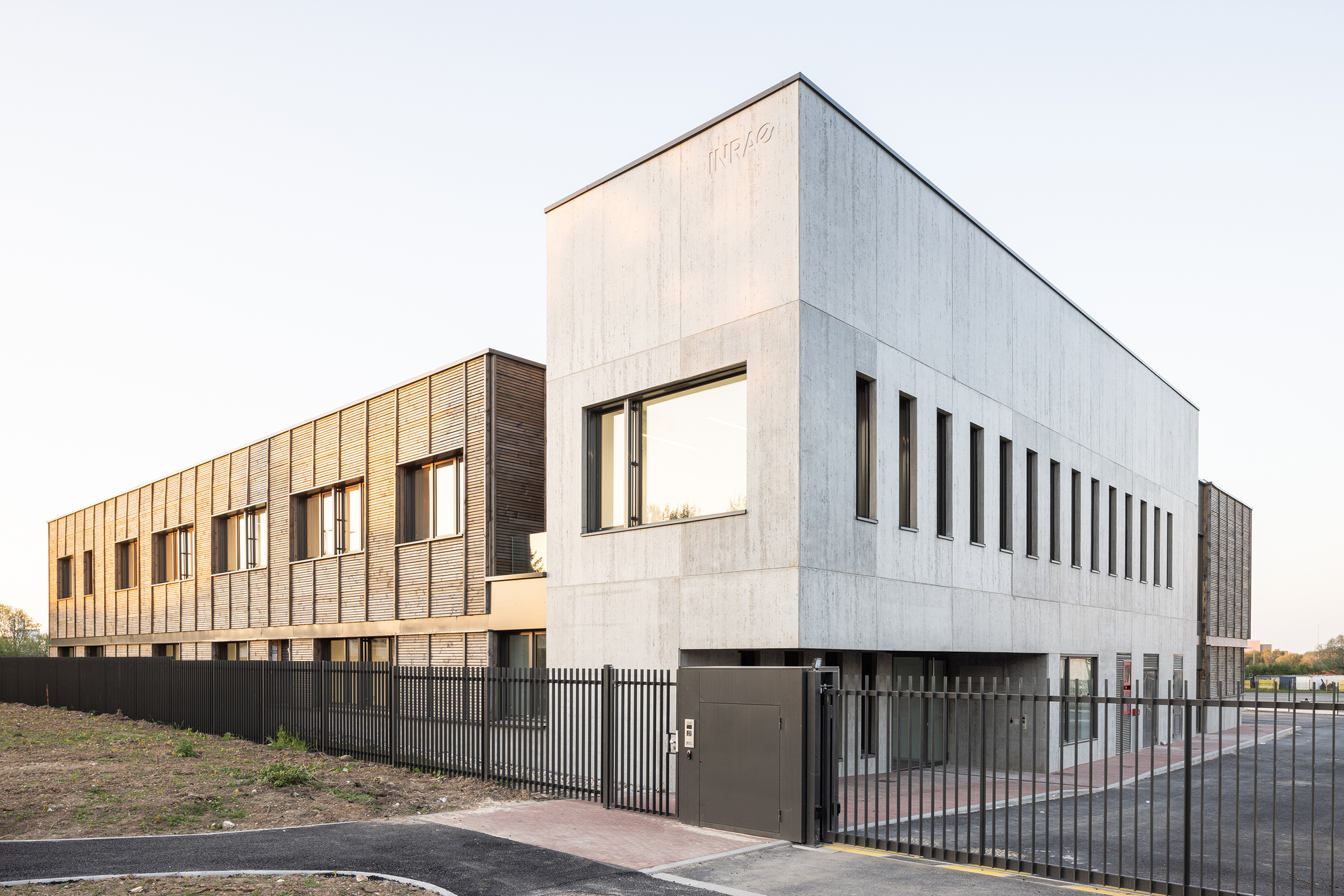 Corner view showing the concrete upper volume with vertical fenestration and dark metal perimeter fence