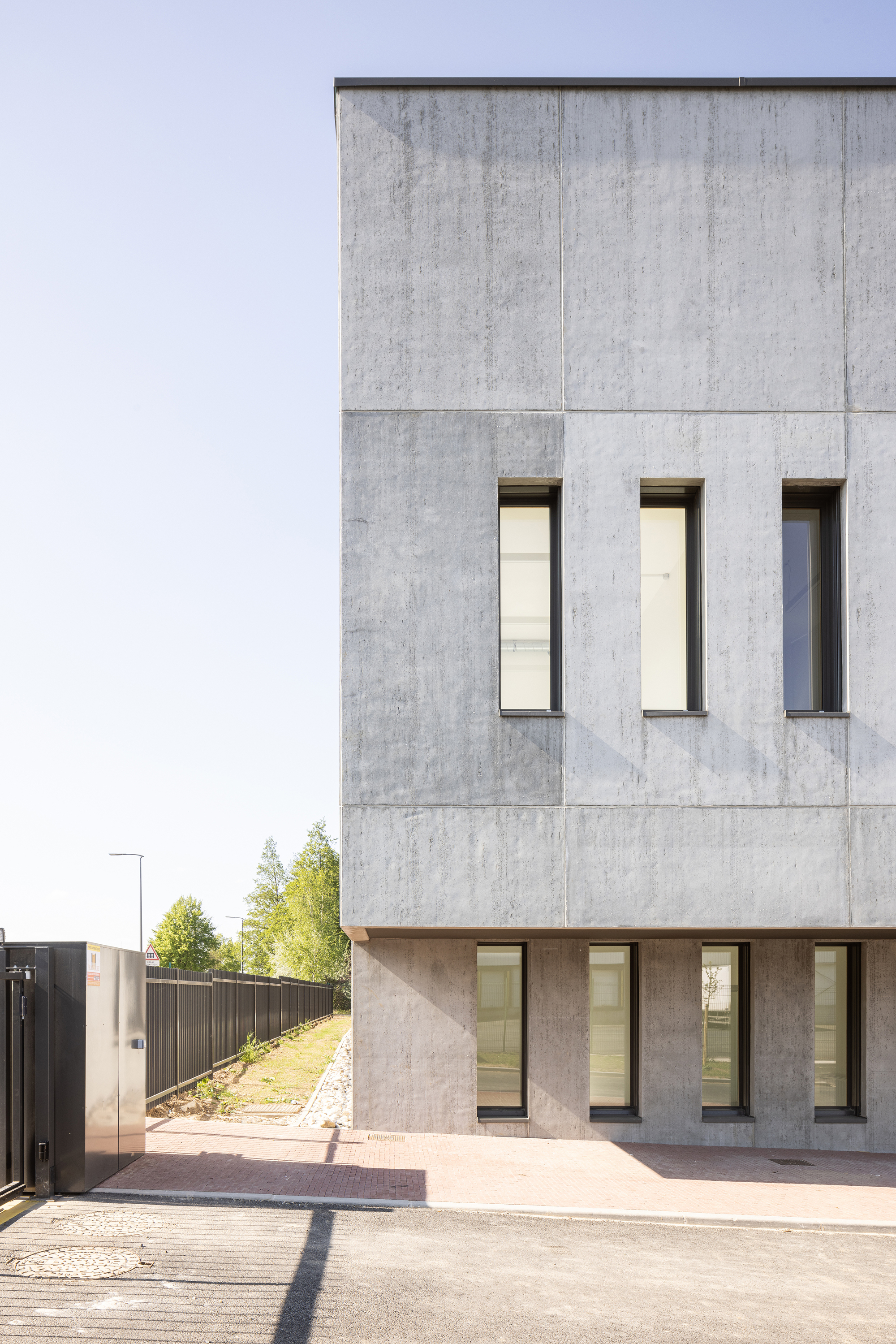 Concrete facade with three vertical windows above a recessed timber-clad ground floor entry in morning light