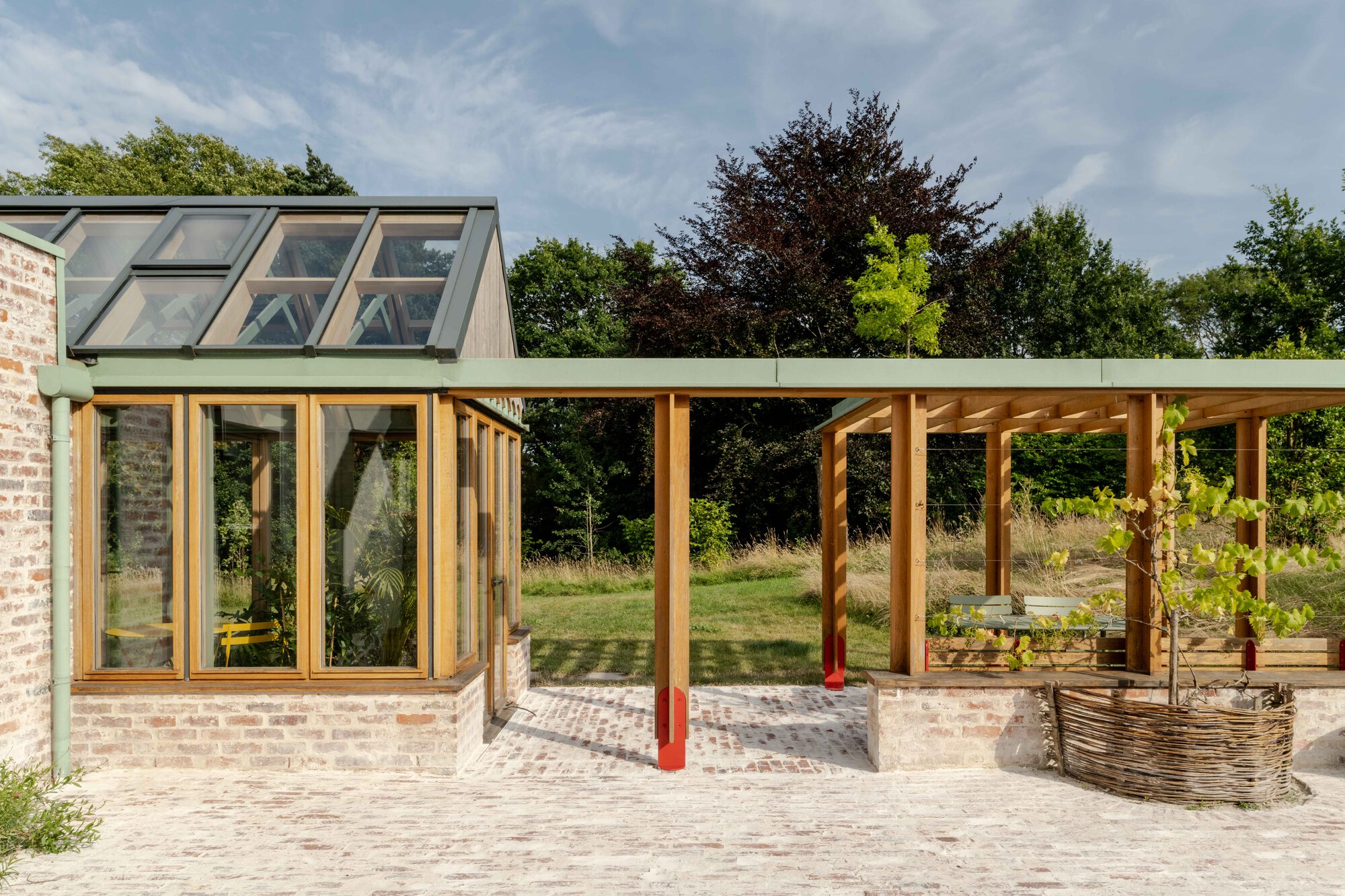 Covered terrace with exposed timber columns and beams extending from a glazed brick pavilion