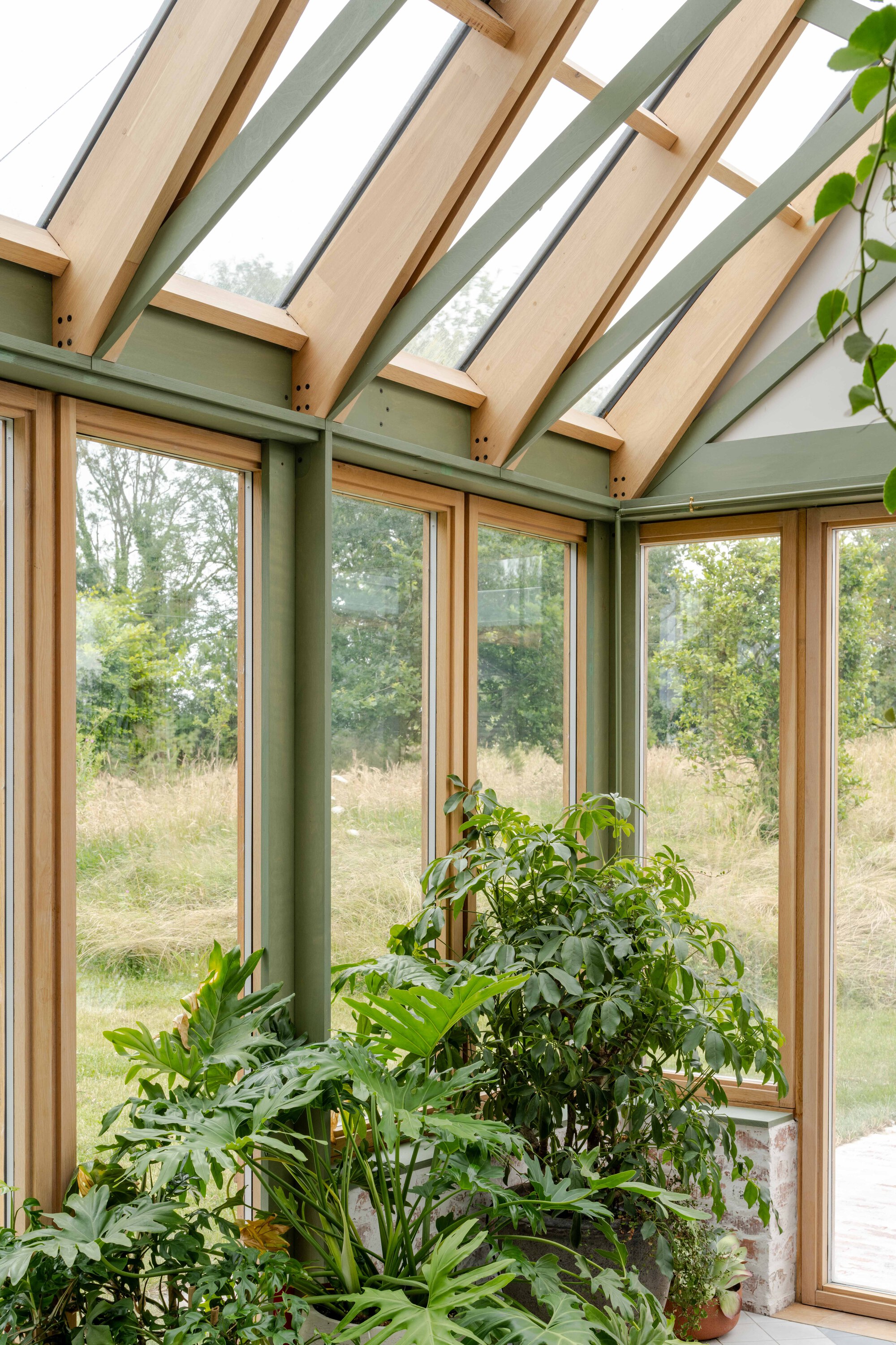 Corner conservatory interior with timber-framed windows, green posts and an array of potted plants