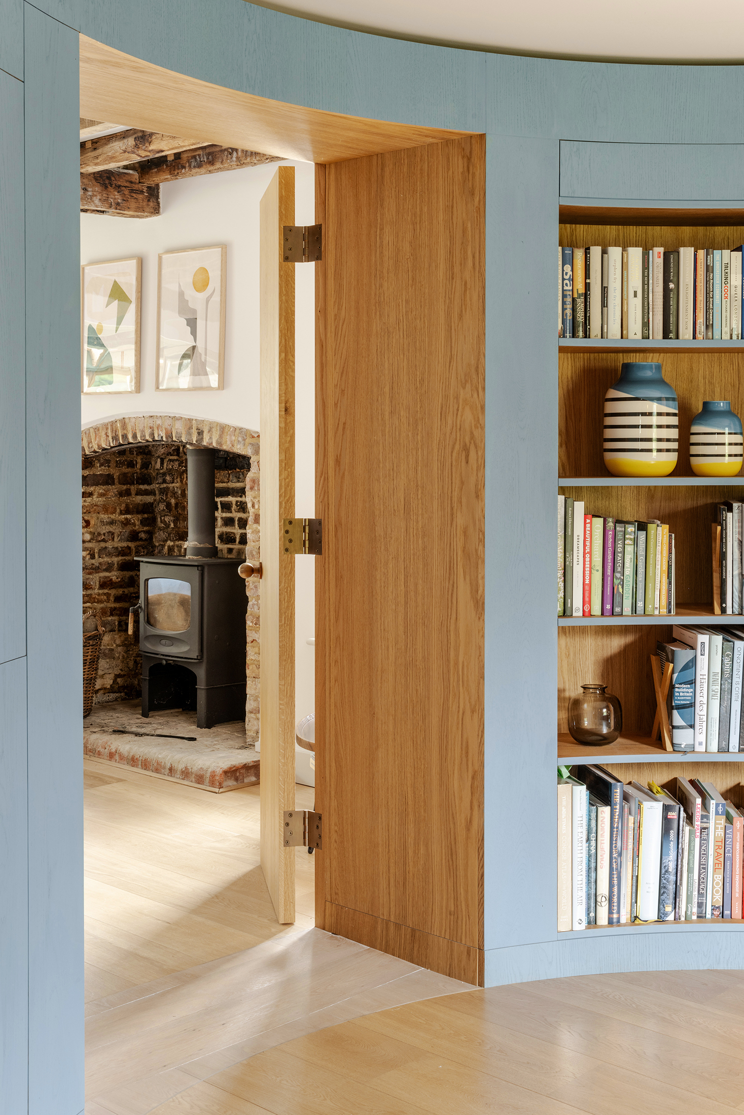 Oak door opening from blue paneled room with built-in shelves to fireplace alcove with exposed brick