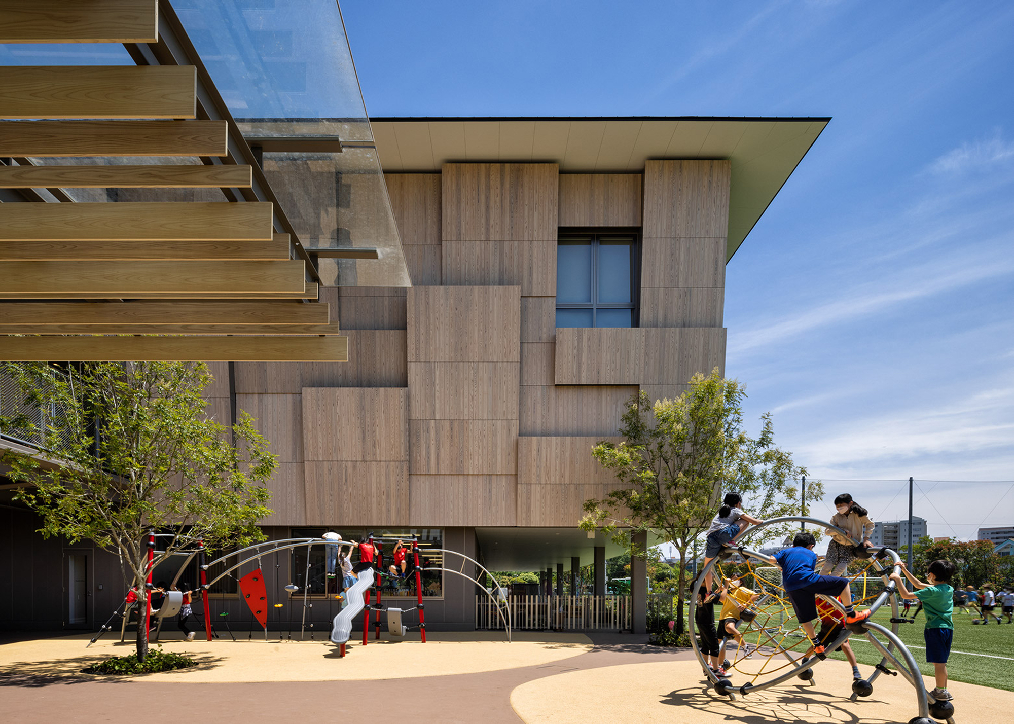 Elevated volume clad in staggered timber panels above a playground with children on climbing equipment