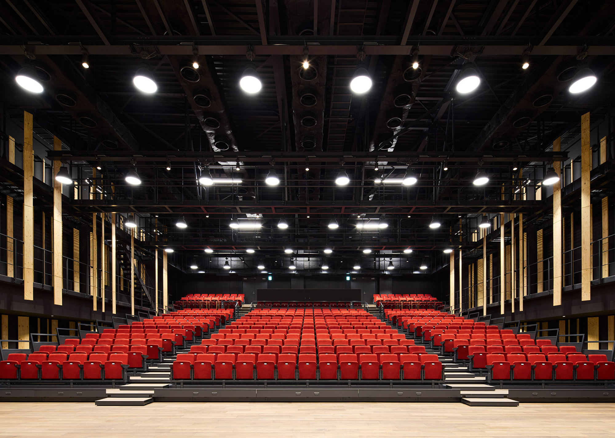 Stage view of auditorium showing symmetric rows of red seats and timber acoustic panels along both walls