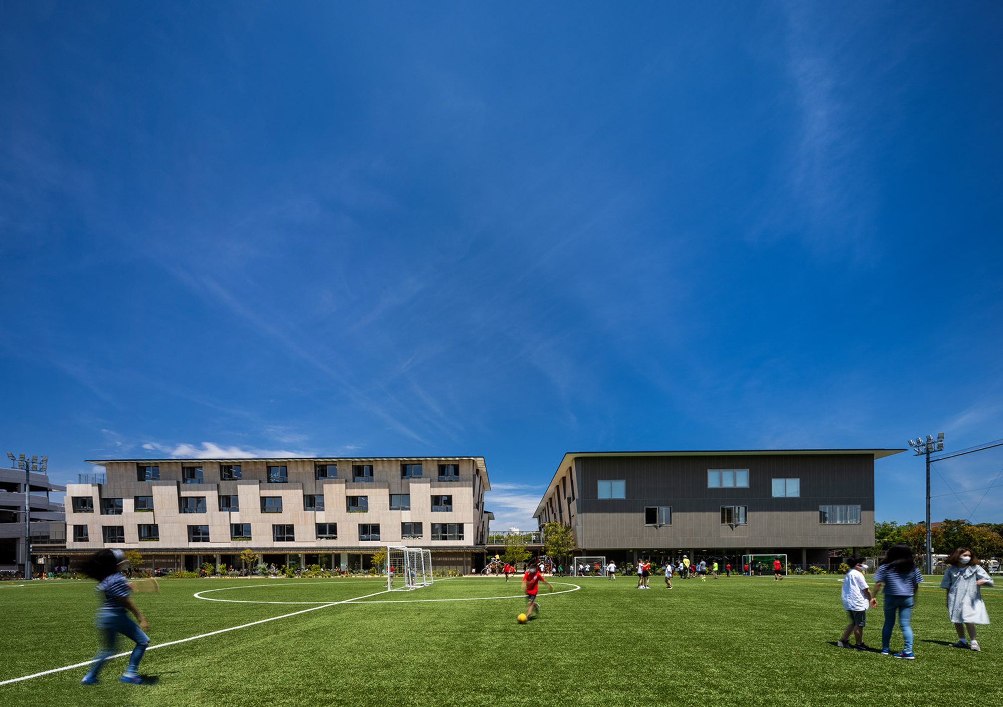 Two residential blocks flanking a sports field with children playing soccer on synthetic turf