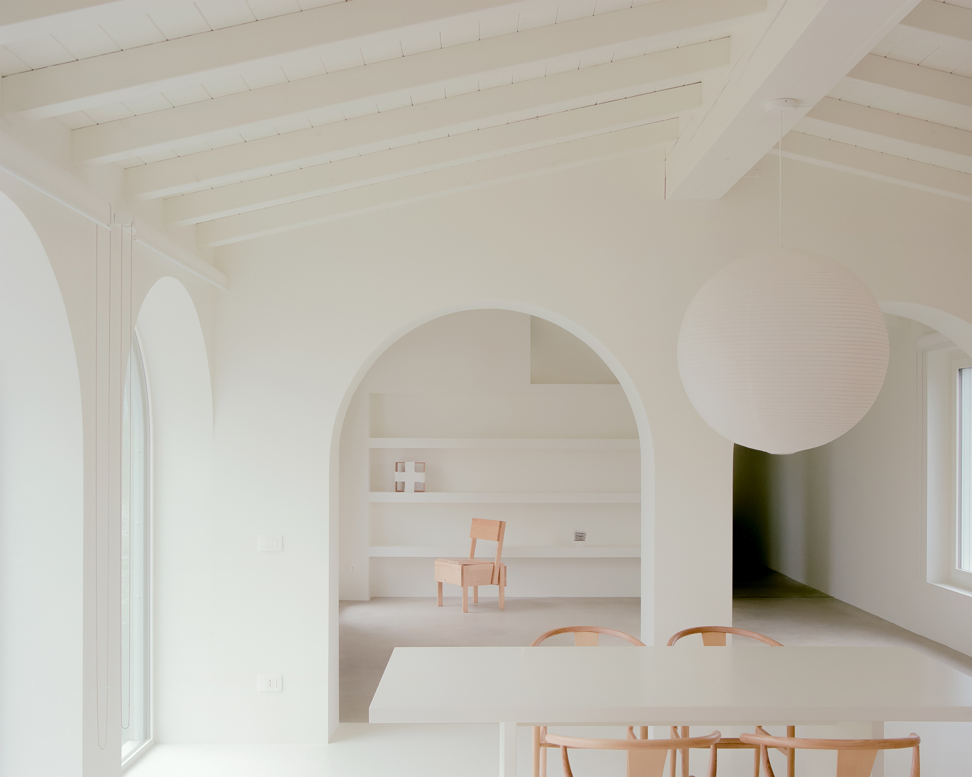 White interior with arched openings connecting dining and living spaces under exposed timber ceiling