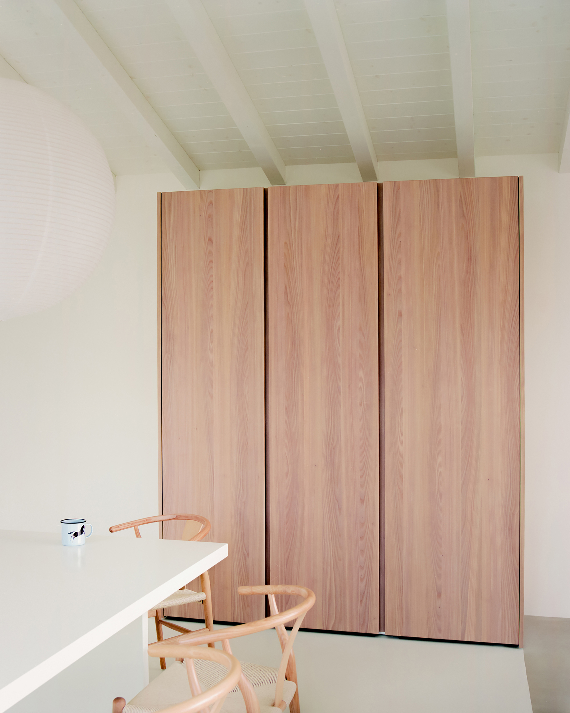 Floor-to-ceiling wardrobe in pale timber veneer beside a white dining table and timber chairs