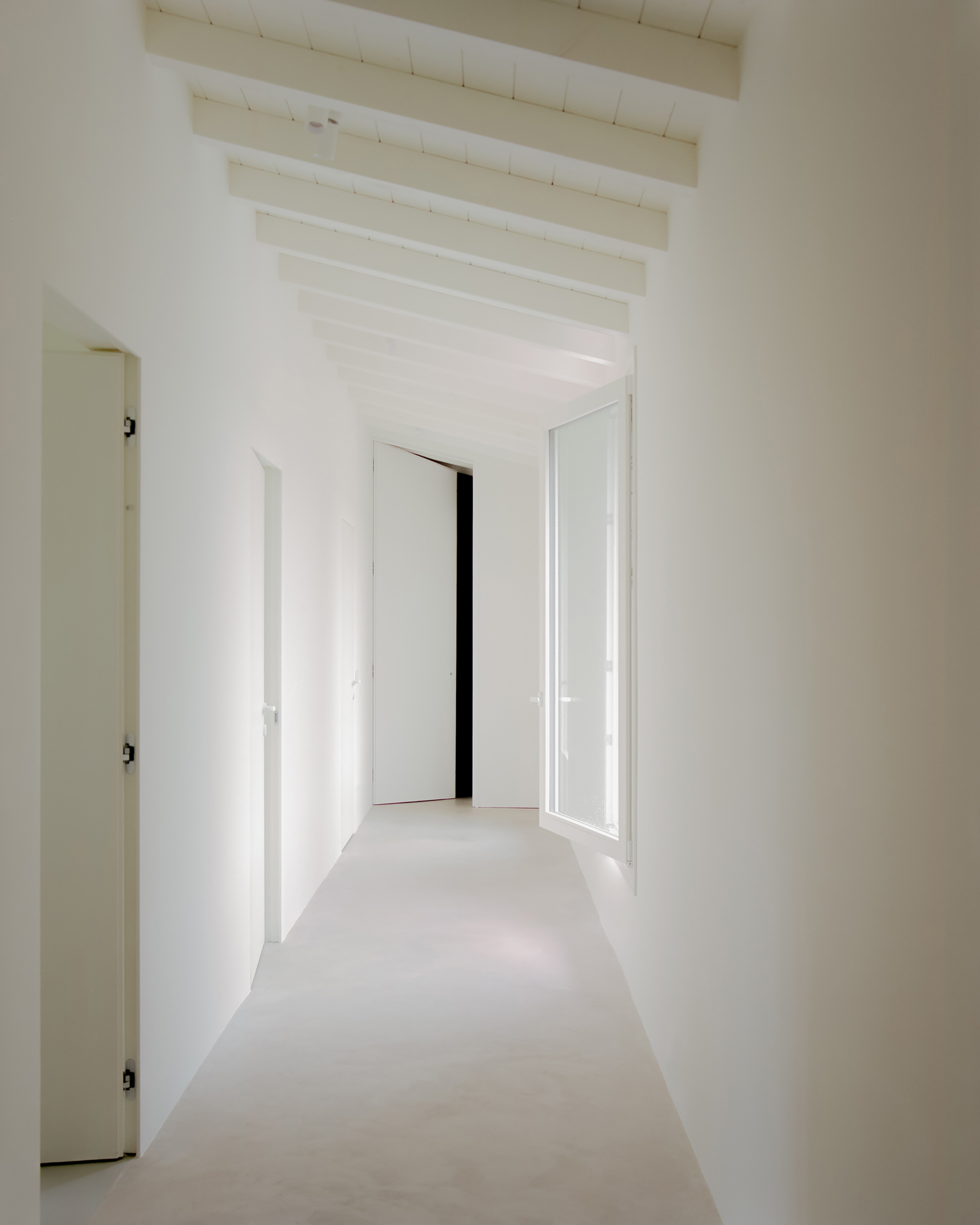 White hallway with exposed timber ceiling joists and open doorways leading to adjacent rooms