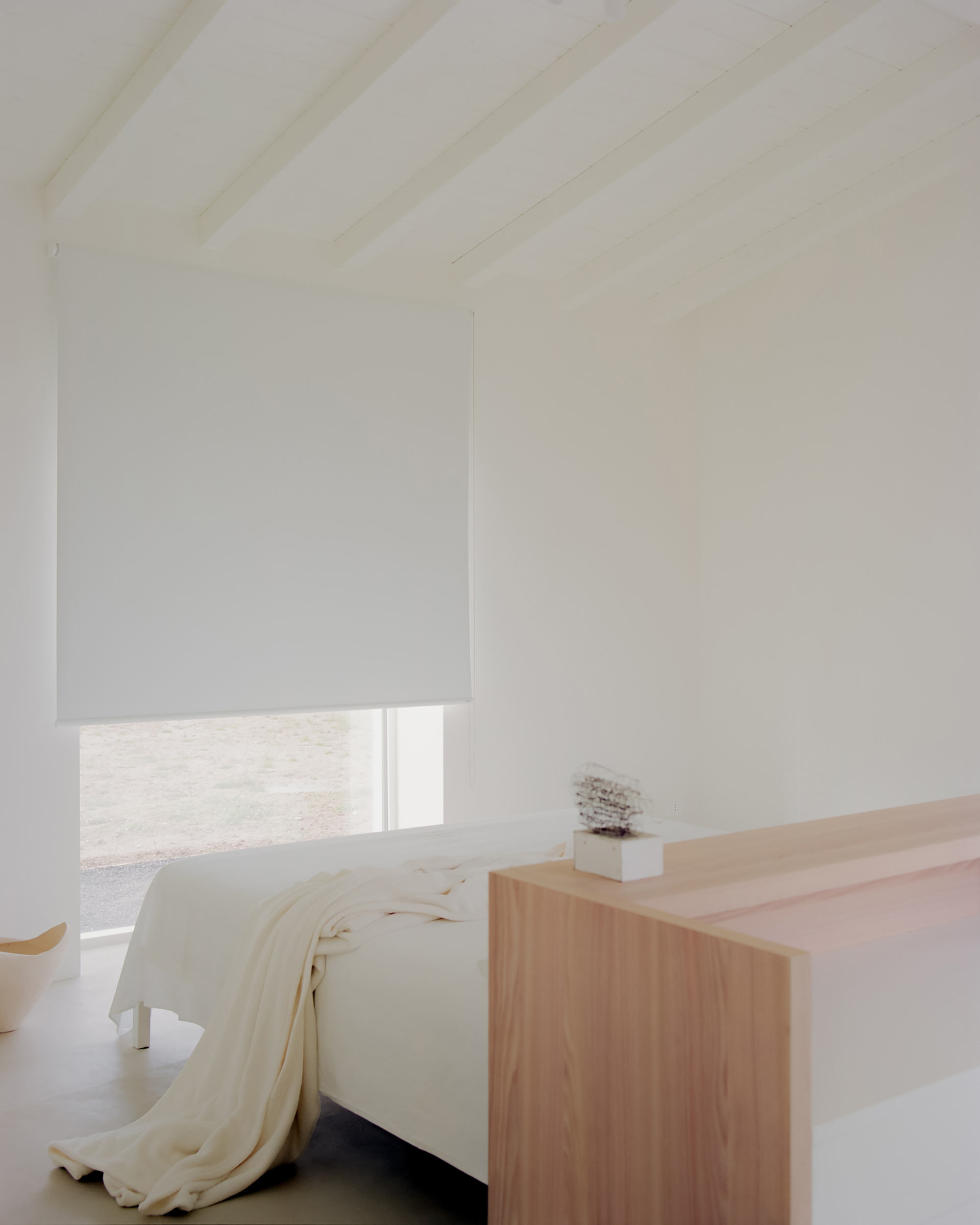 Bedroom with a pale timber headboard wall and a window fitted with a white roller shade