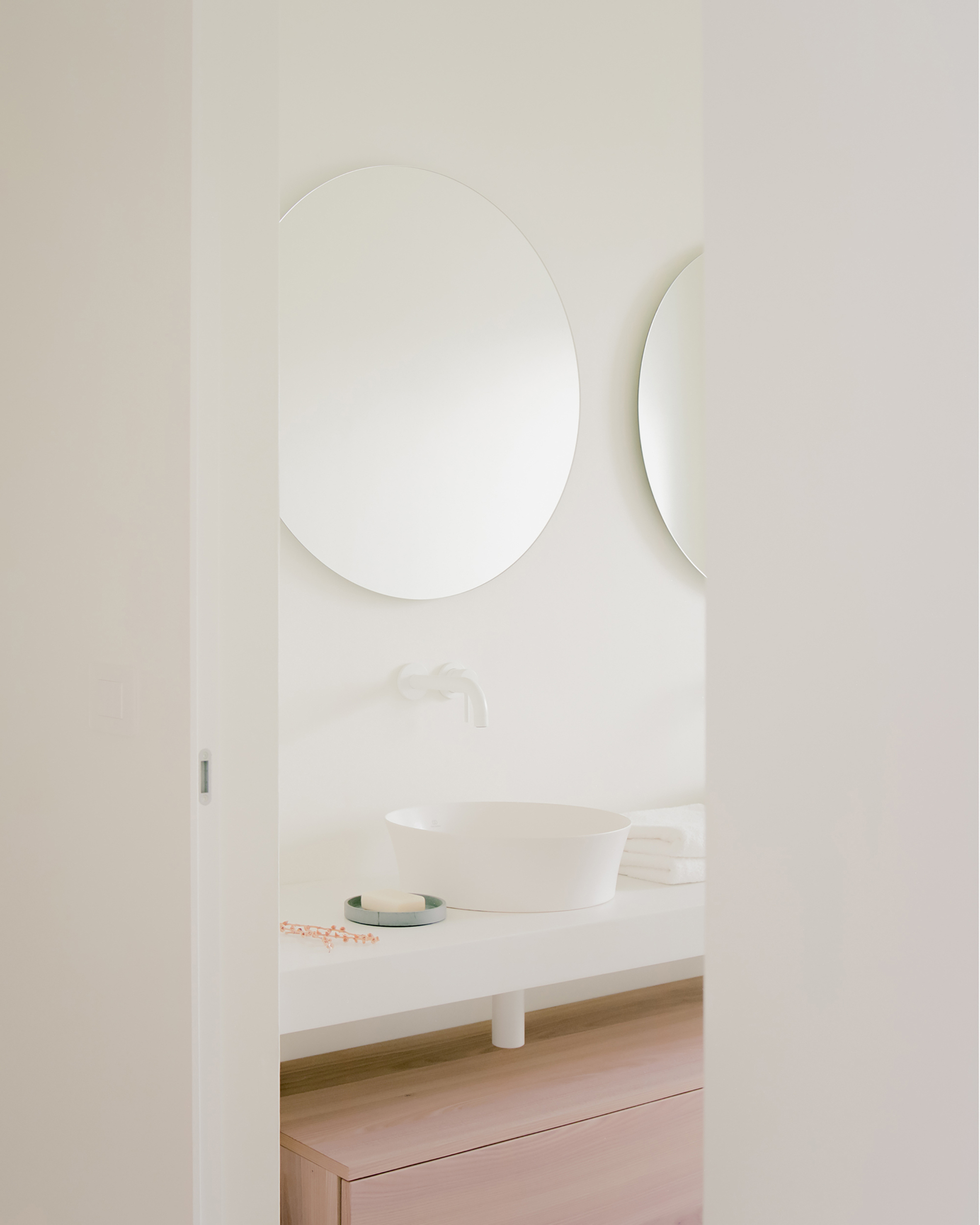 Oval mirror and curved wall-mounted shelf above a vessel sink on pale counter