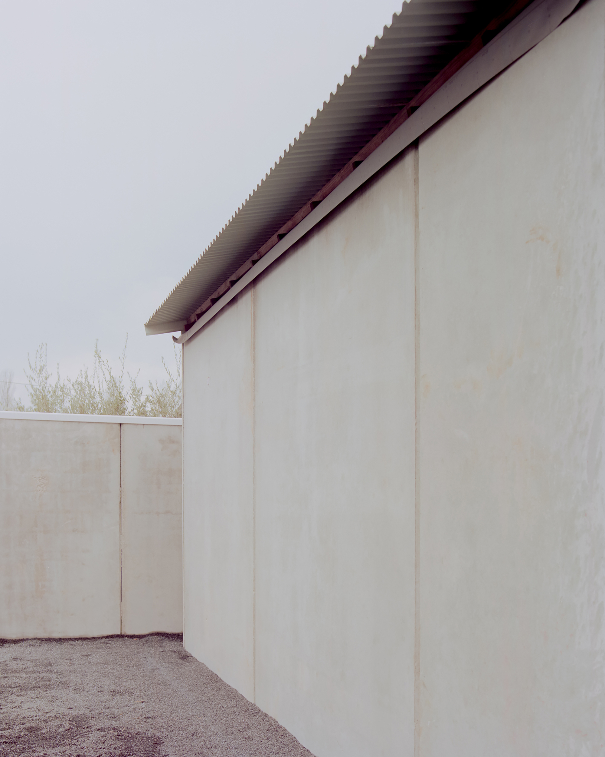 Corner detail of plastered walls with exposed corrugated metal roof eave under overcast sky