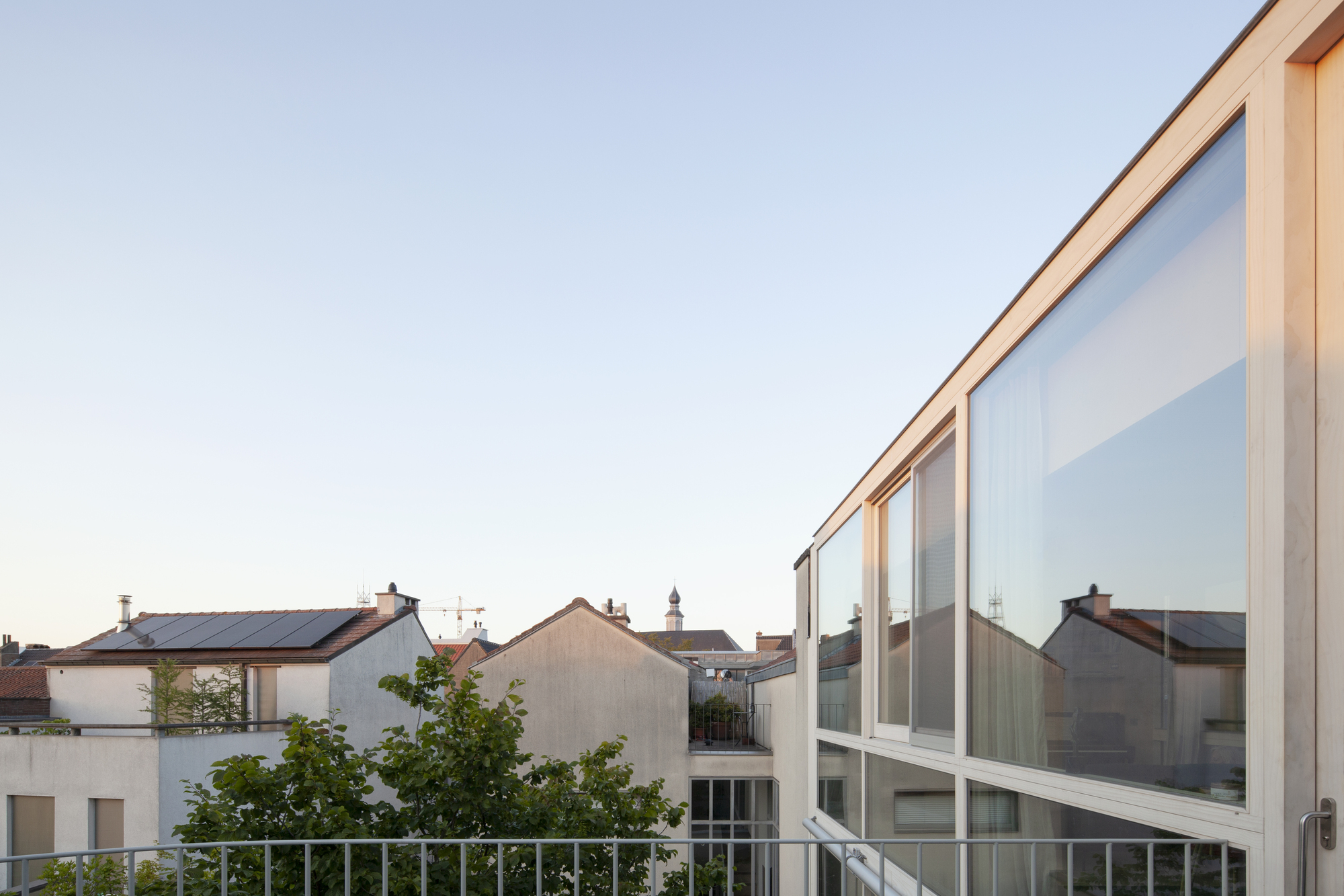 Timber-framed glazed upper level with white railing overlooking neighboring rooftops at sunset