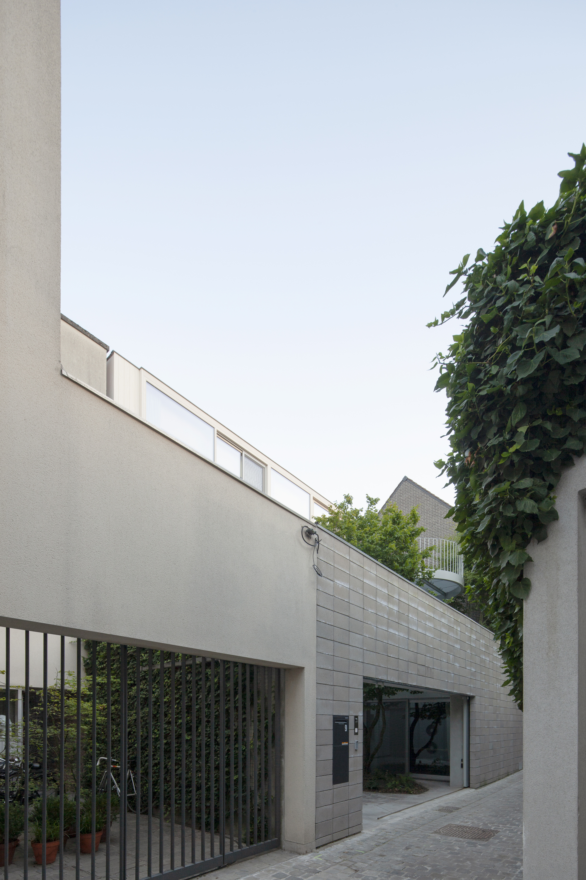 Street view of white block volumes and grey tile wall between ivy-covered neighbors