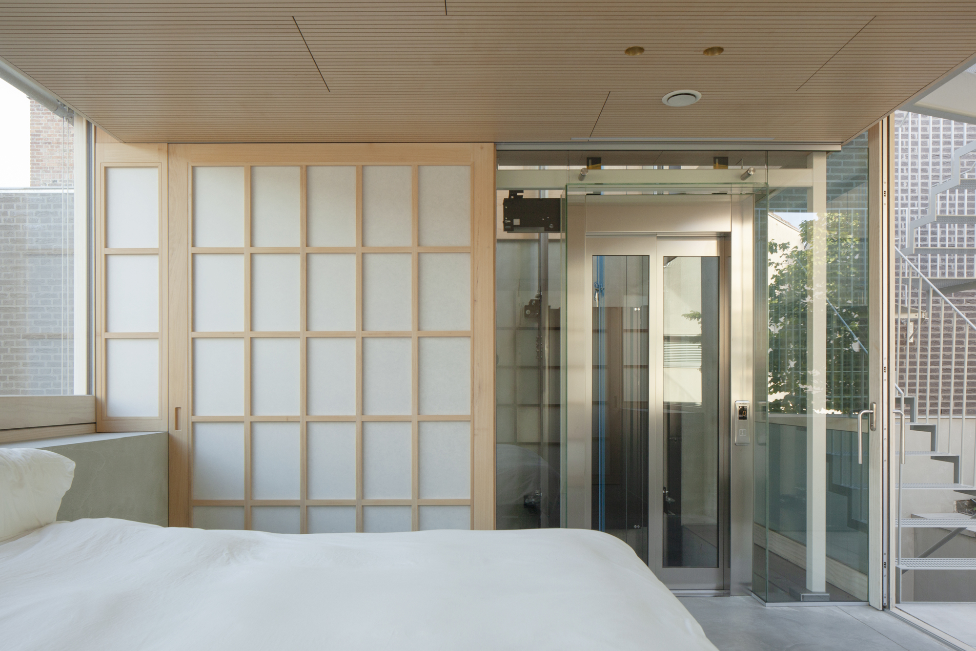 Bedroom with translucent sliding shoji screens and glass shower enclosure beneath a timber slatted ceiling