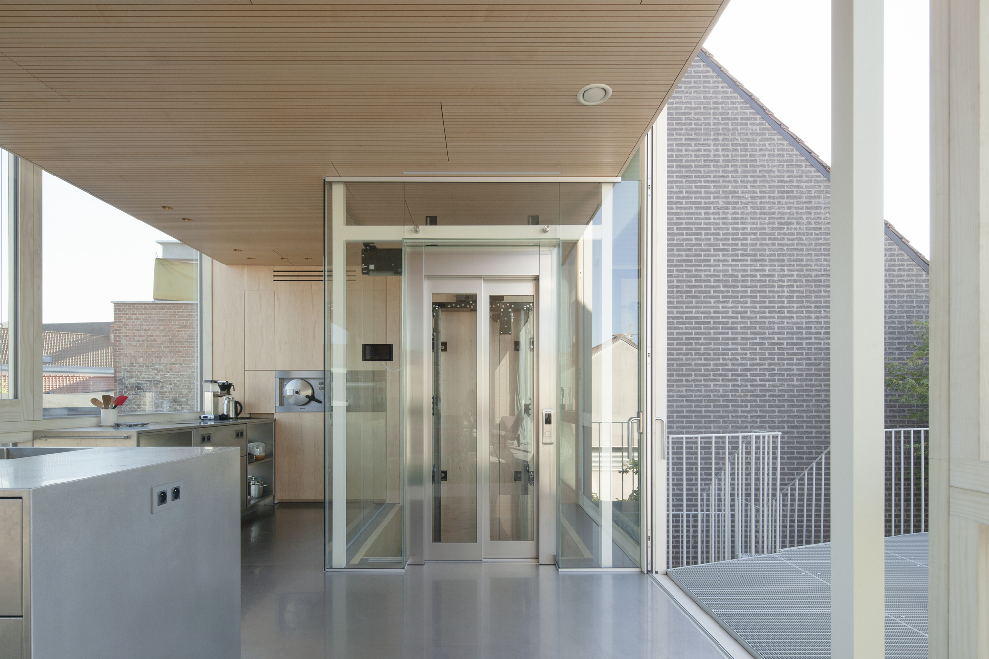 Kitchen with glass elevator shaft opening to balcony overlooking neighboring brick facades