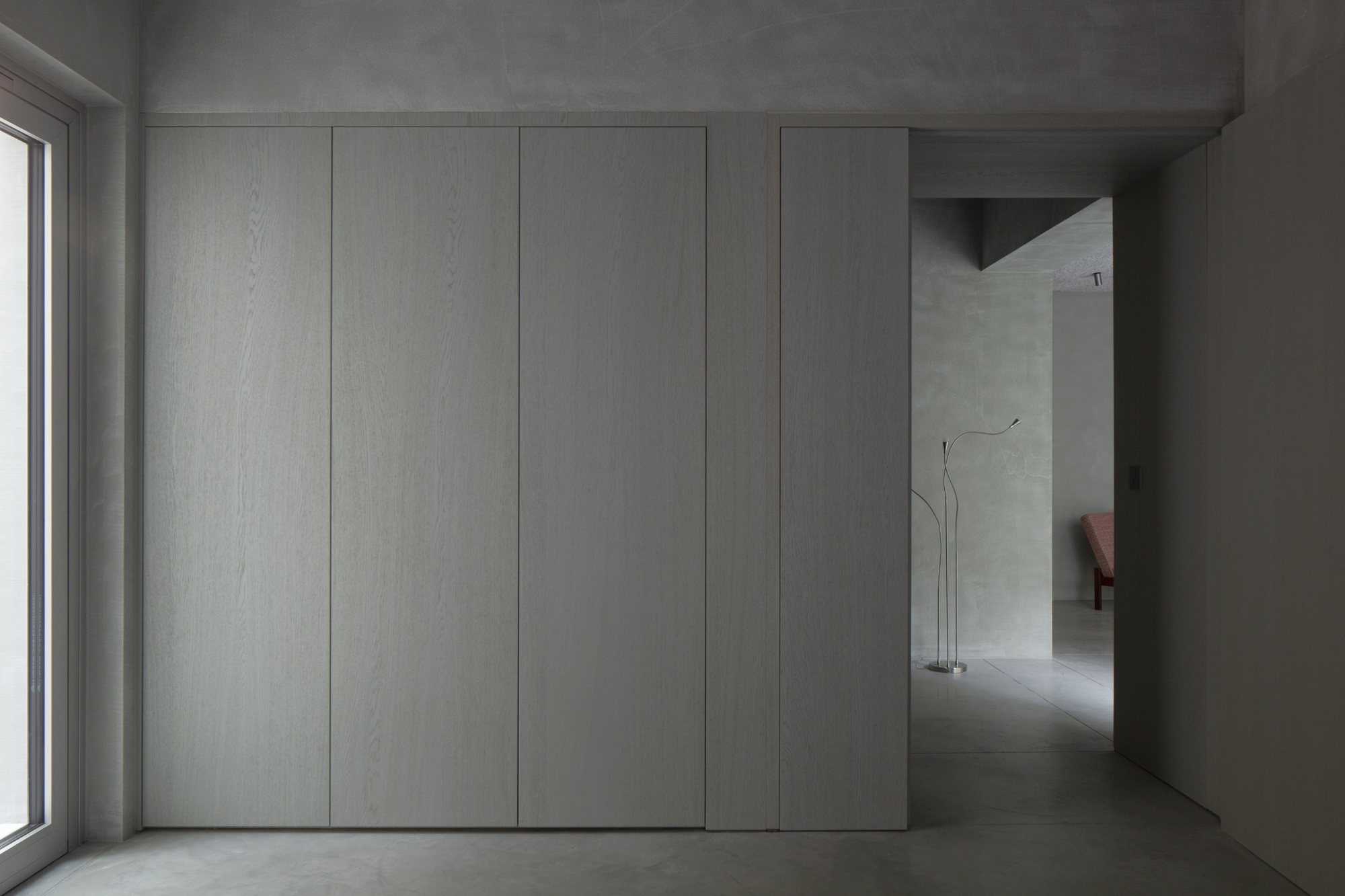 Flush white paneled wall with concealed joints adjacent to concrete floor and window