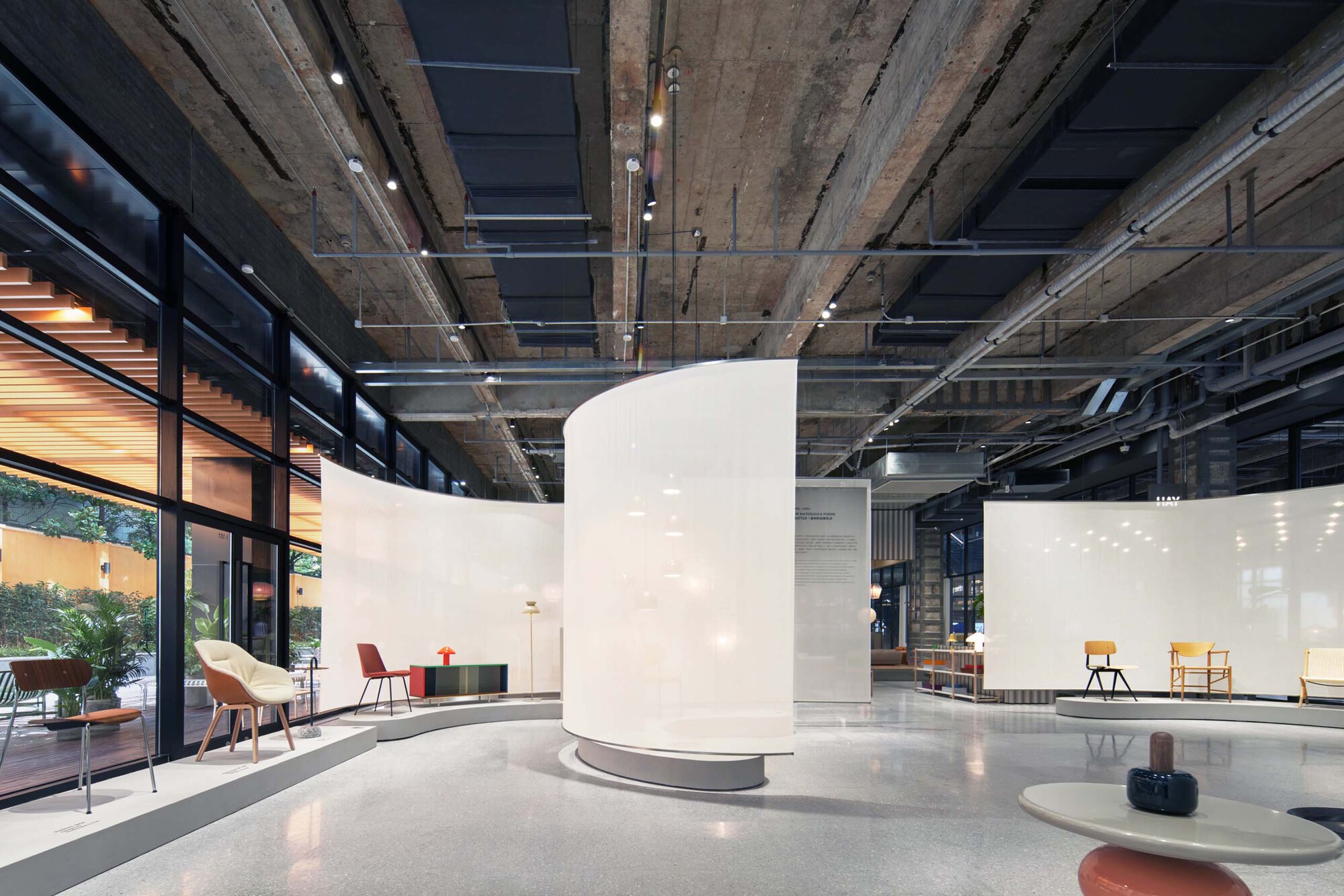 Curved white partition wall in open interior with exposed concrete ceiling and floor-to-ceiling windows