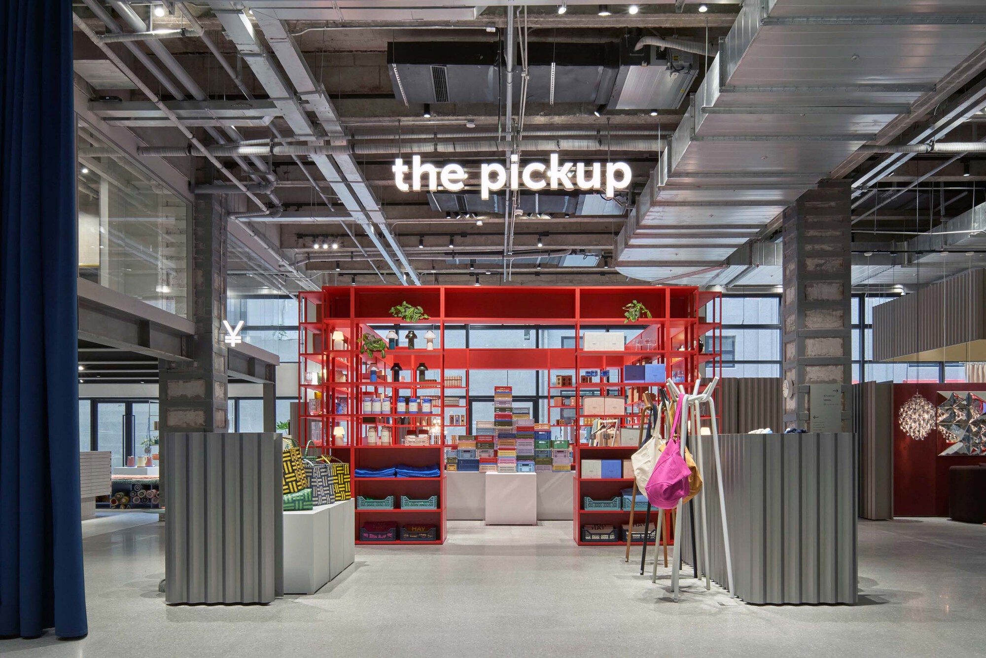 Red metal shelving unit with corrugated metal screens beneath exposed concrete ceiling and visible mechanical systems