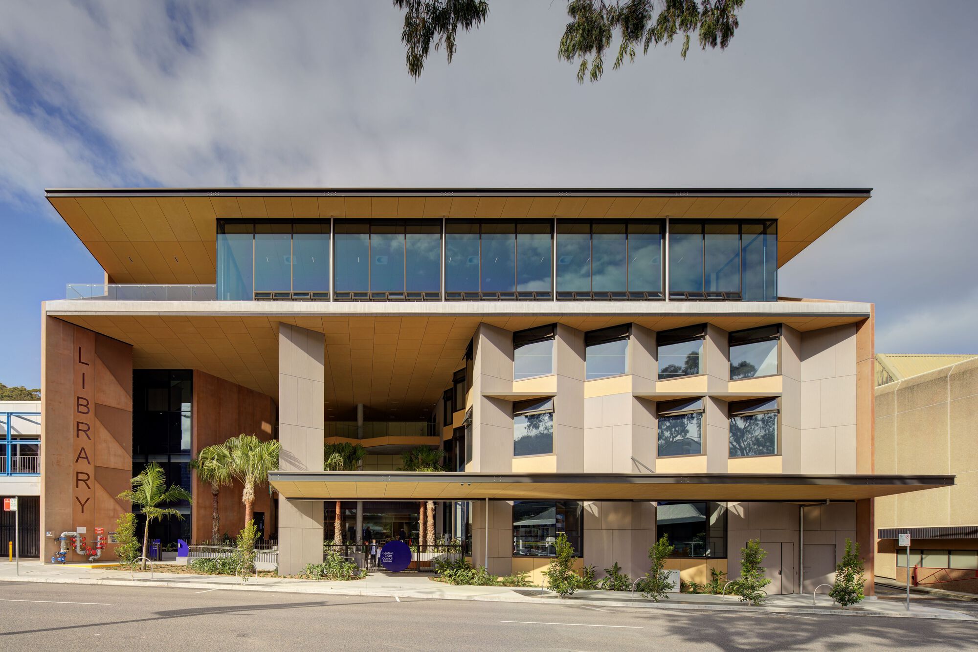 Street view of the cantilevered facade with timber soffits and full-height glazing under cloudy skies