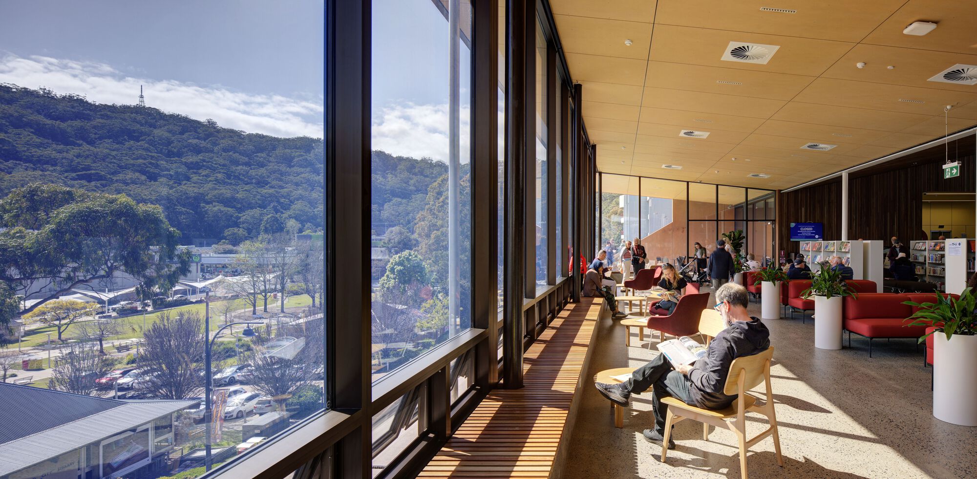 Reading room with floor-to-ceiling windows overlooking hillside parkland in afternoon light