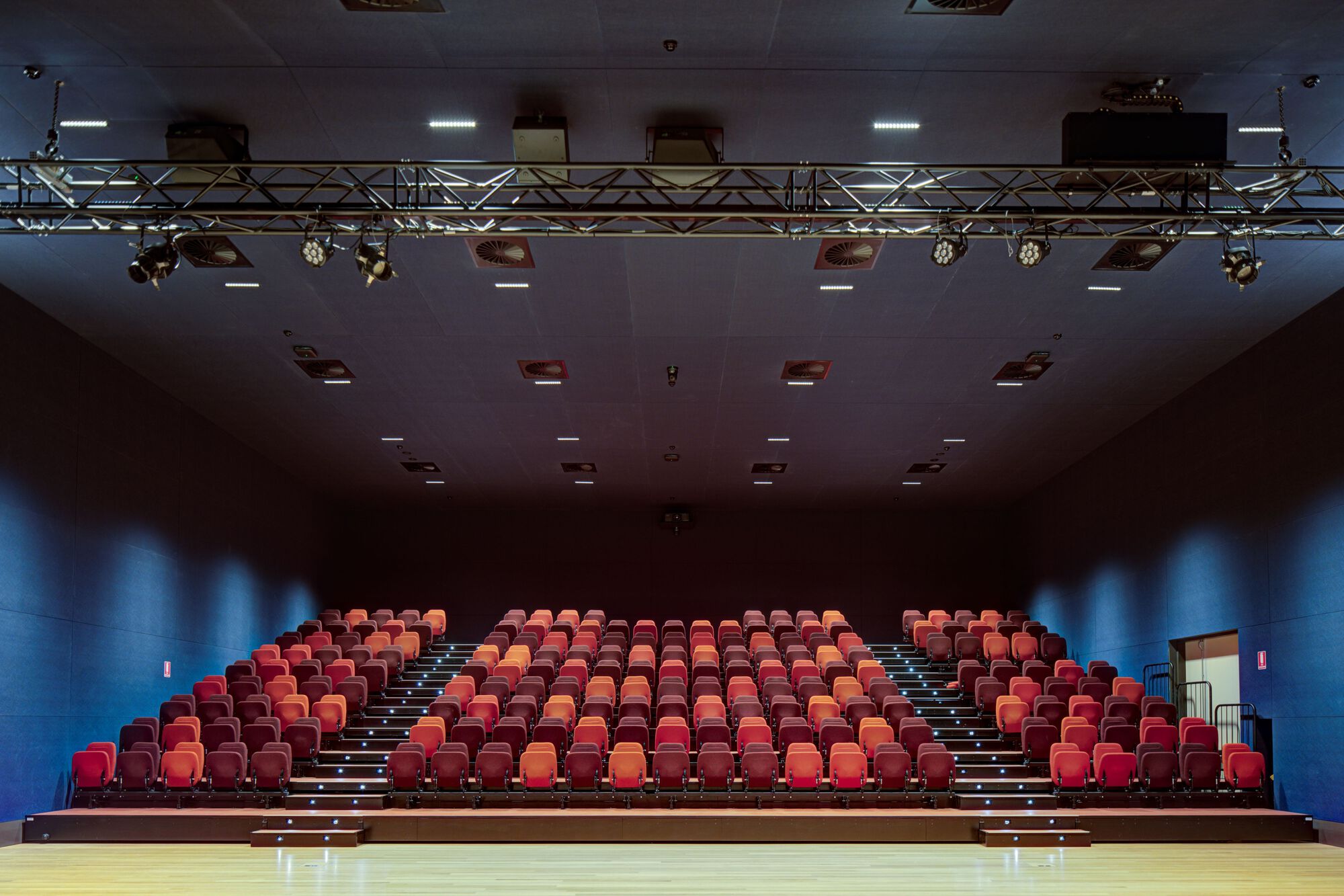 Auditorium seating in red and orange upholstery with theatrical lighting rig overhead