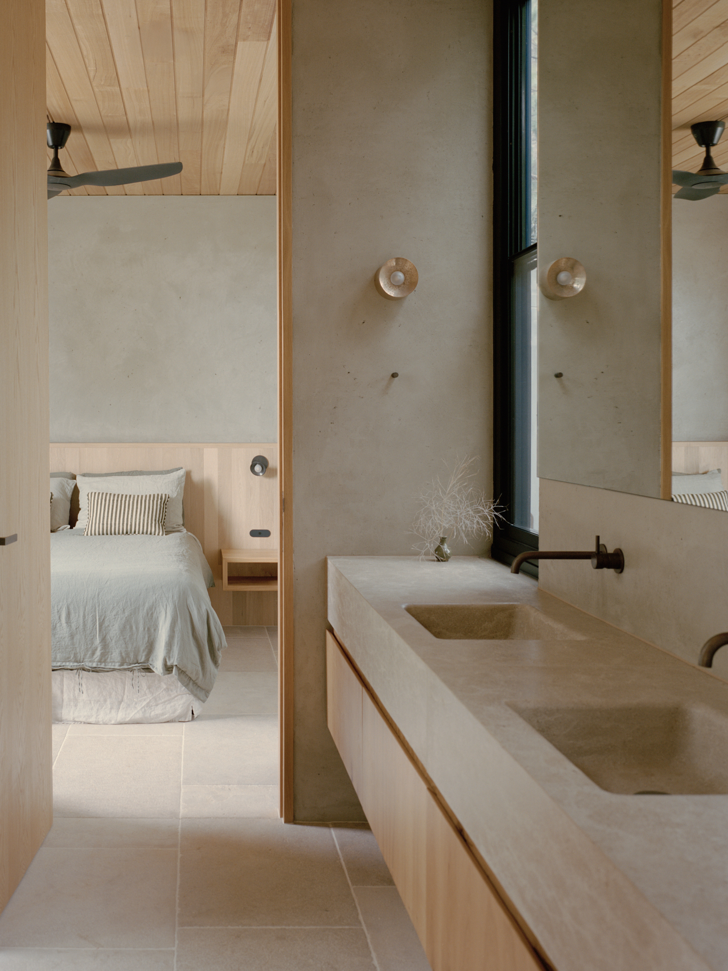 Ensuite bathroom with limestone vanity and vertical mirror reflecting bedroom through timber-framed doorway