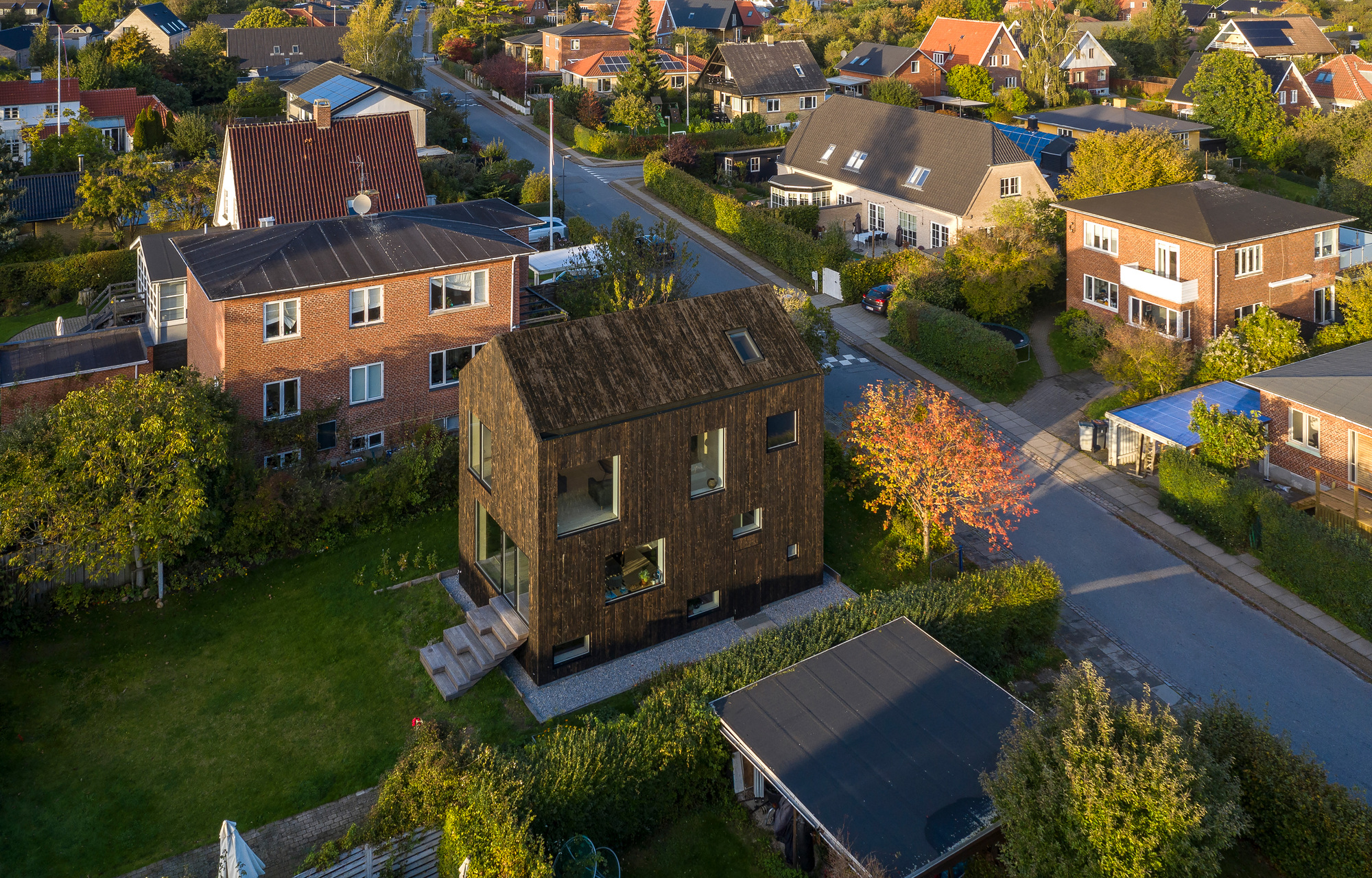 Aerial view of the timber-clad house nestled among neighboring buildings with an autumn tree in front