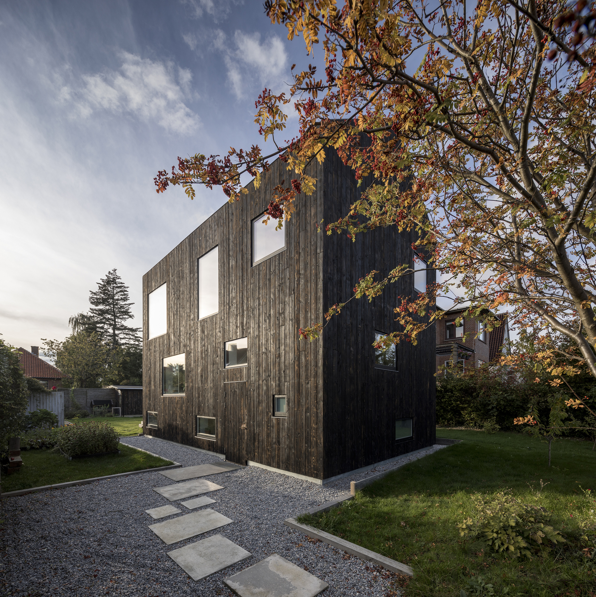Side elevation showing vertically cladded timber volume with scattered window openings framed by autumn branches