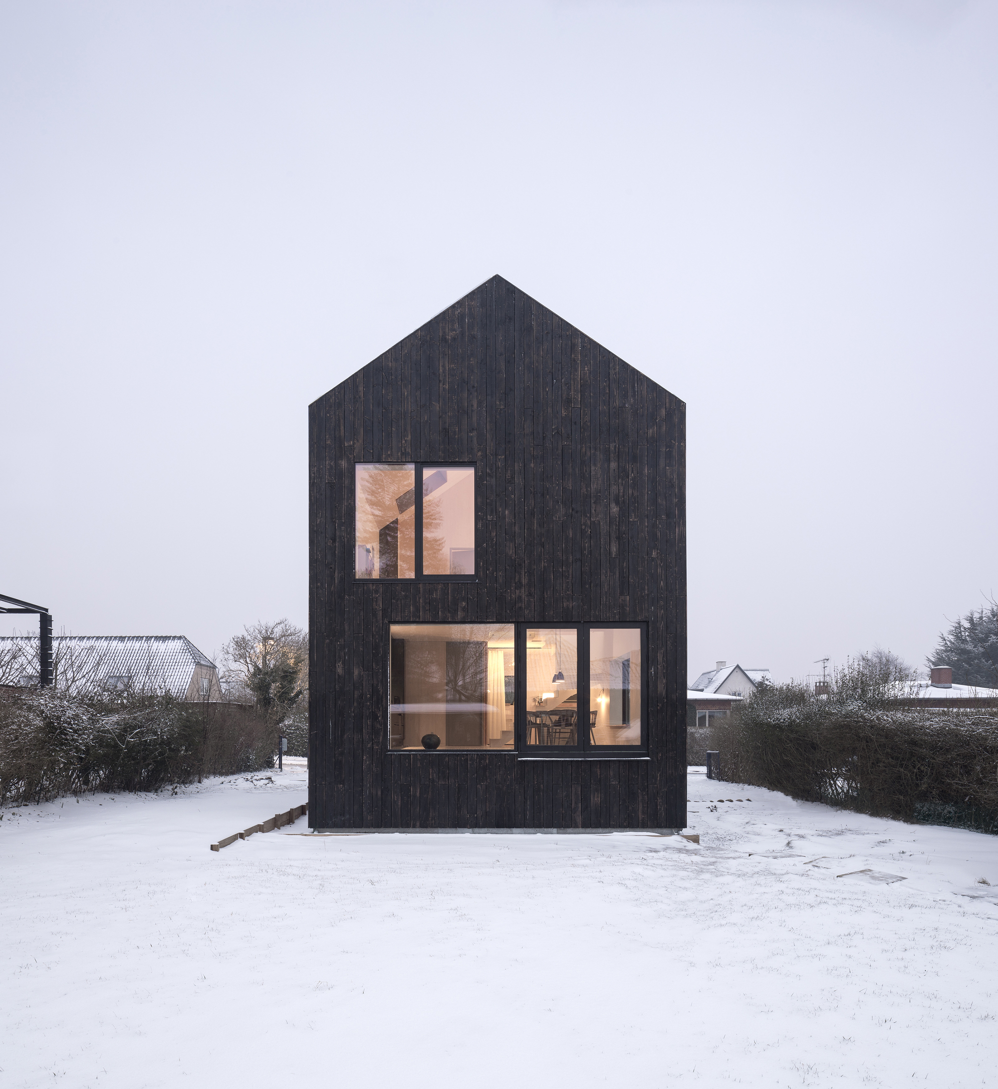 Gable-fronted elevation with charred timber cladding and large glazed openings in a snowy landscape