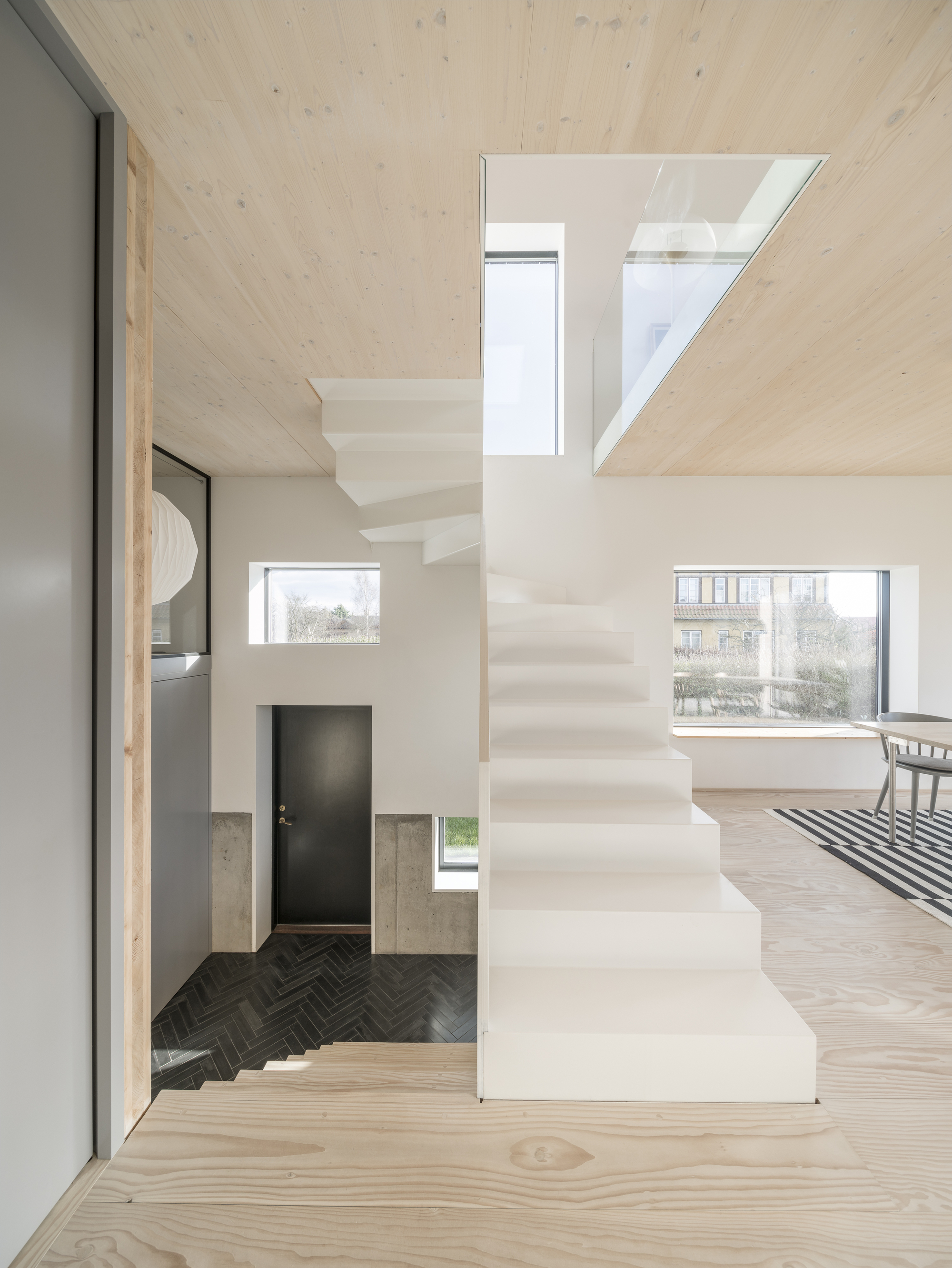 Double-height interior with white folded staircase connecting split levels under a light wood ceiling