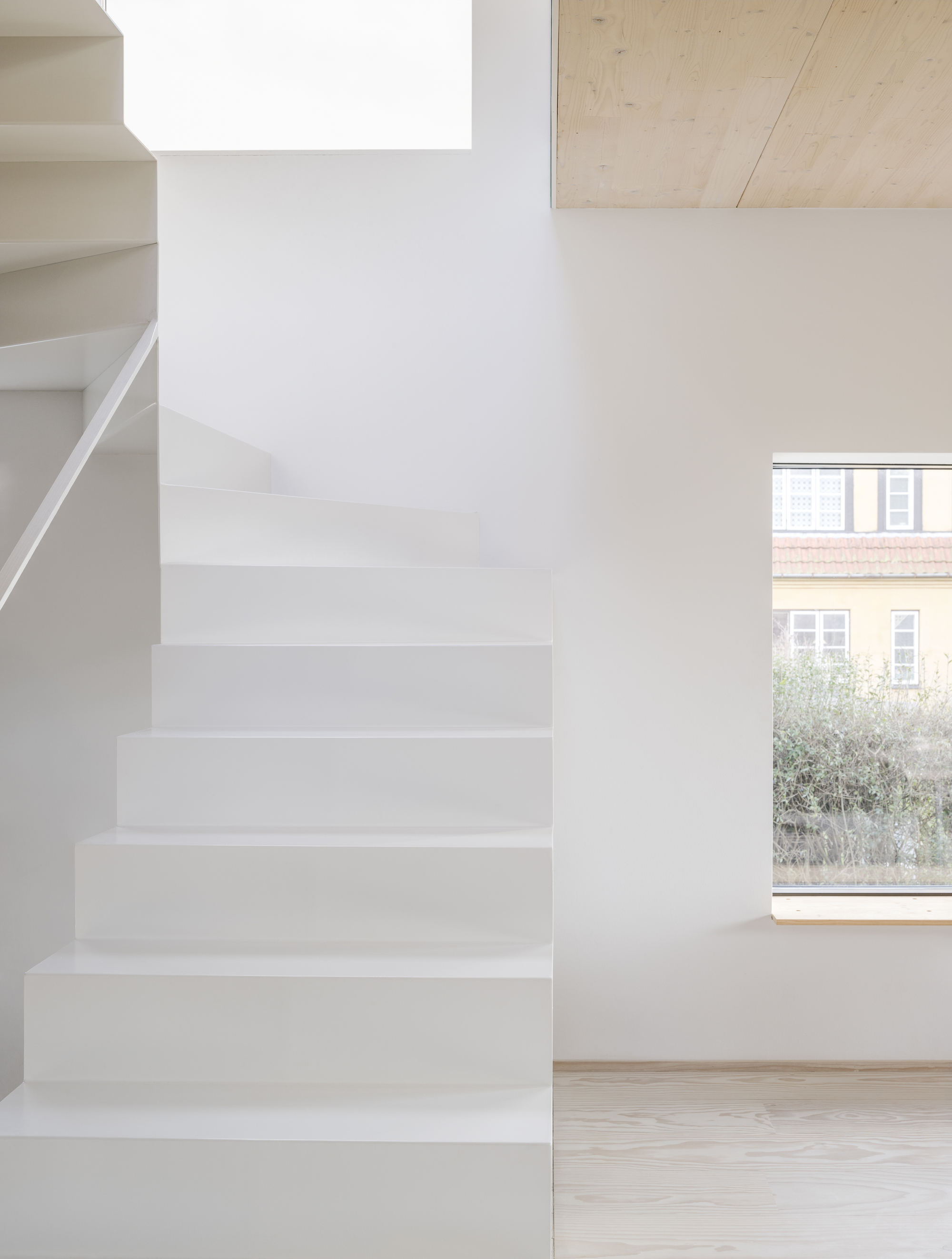 White plastered staircase next to a window overlooking neighboring brick buildings