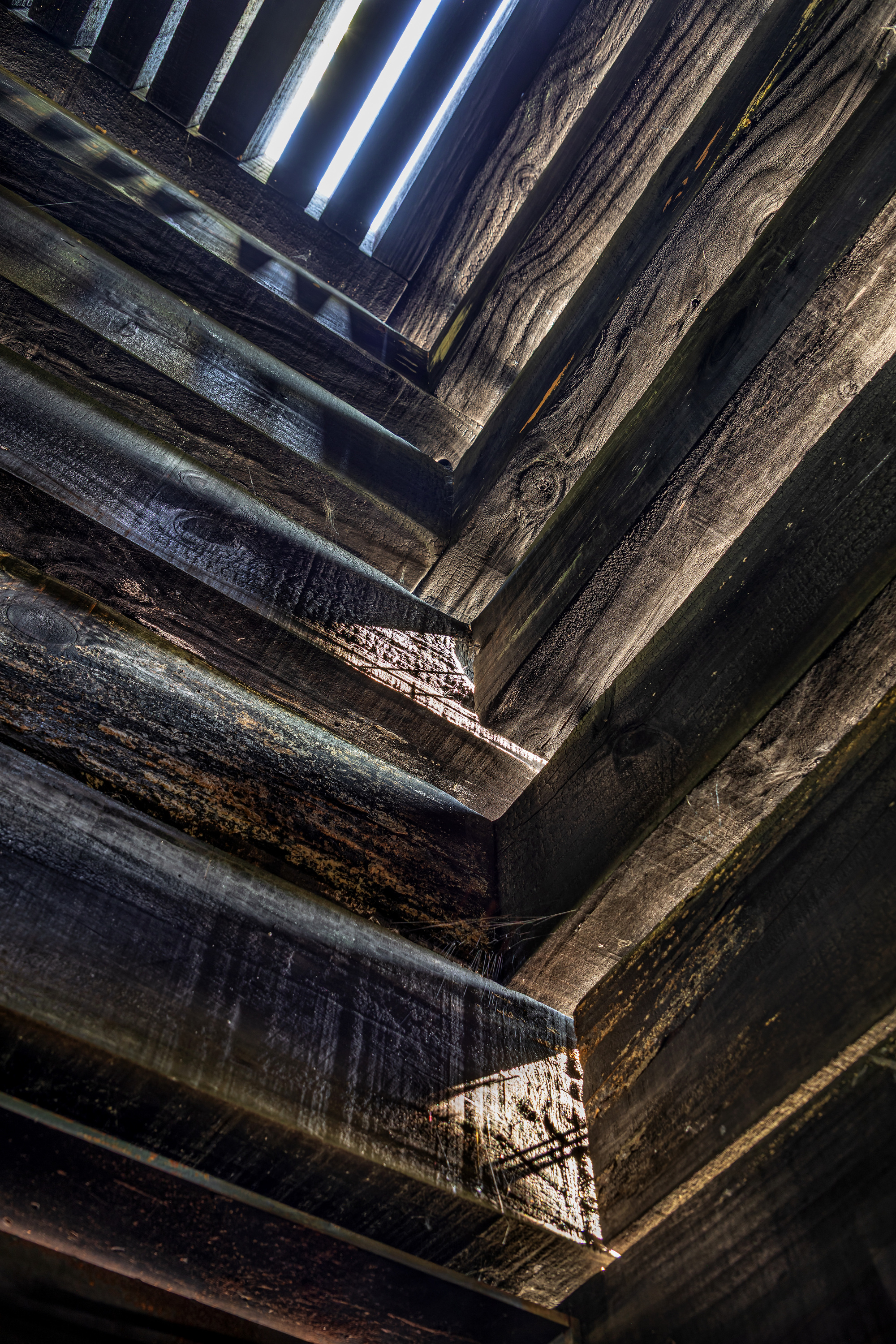 Angled view up interior shaft showing charred timber walls and daylight gaps between boards