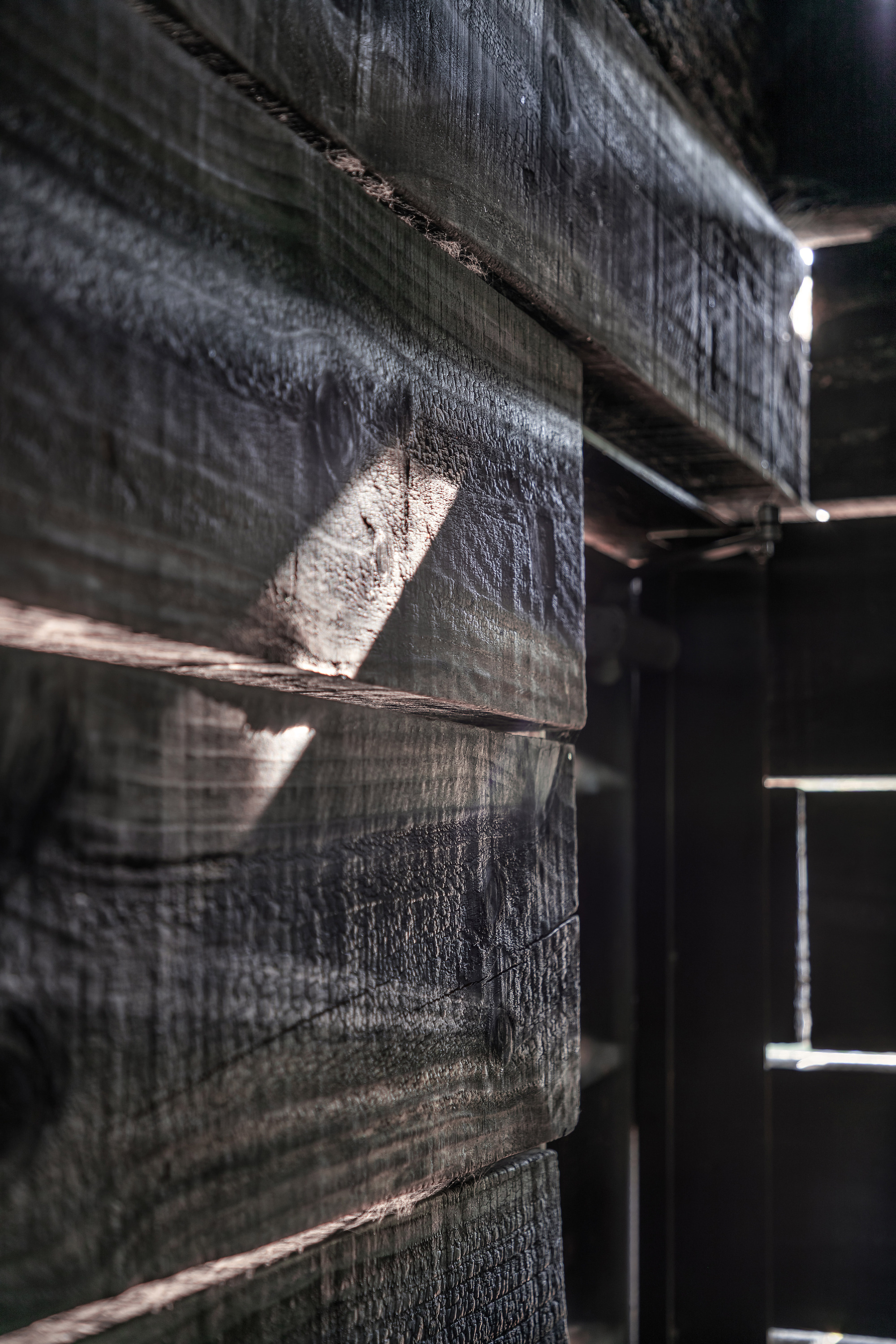 Close-up of charred timber beams with horizontal gaps allowing daylight to penetrate through the structure