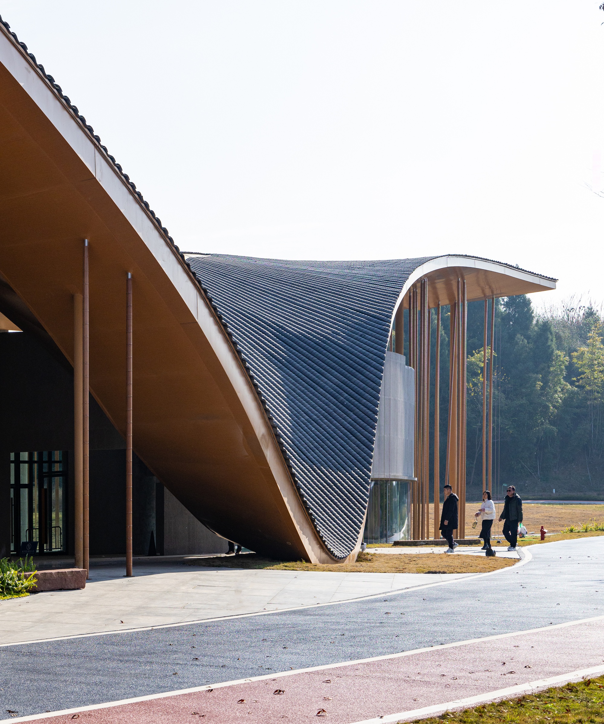 Entrance facade showing the swooping roof soffit and vertical tube screen with visitors walking beneath