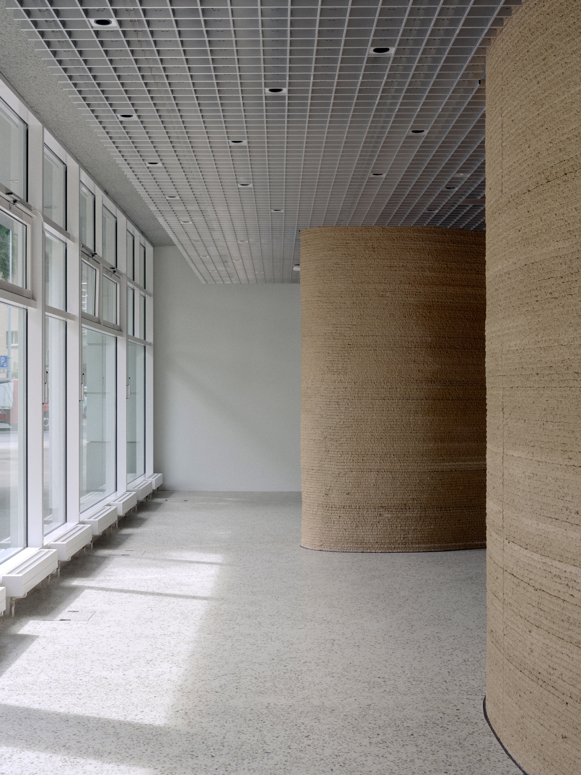 Curved timber-wrapped columns flanking glazed facade with filtered daylight on terrazzo floor