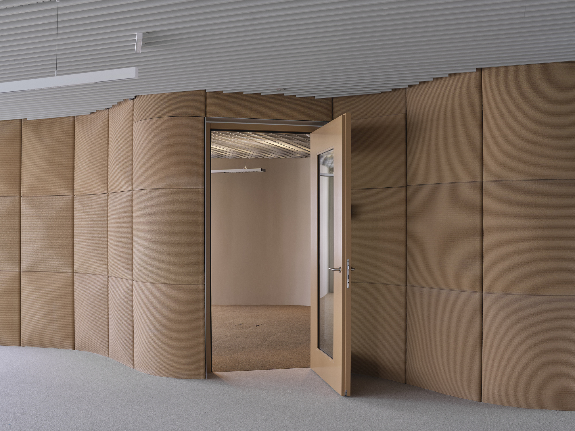 Open double doors in a curved copper-paneled wall revealing an empty room with ribbed ceiling