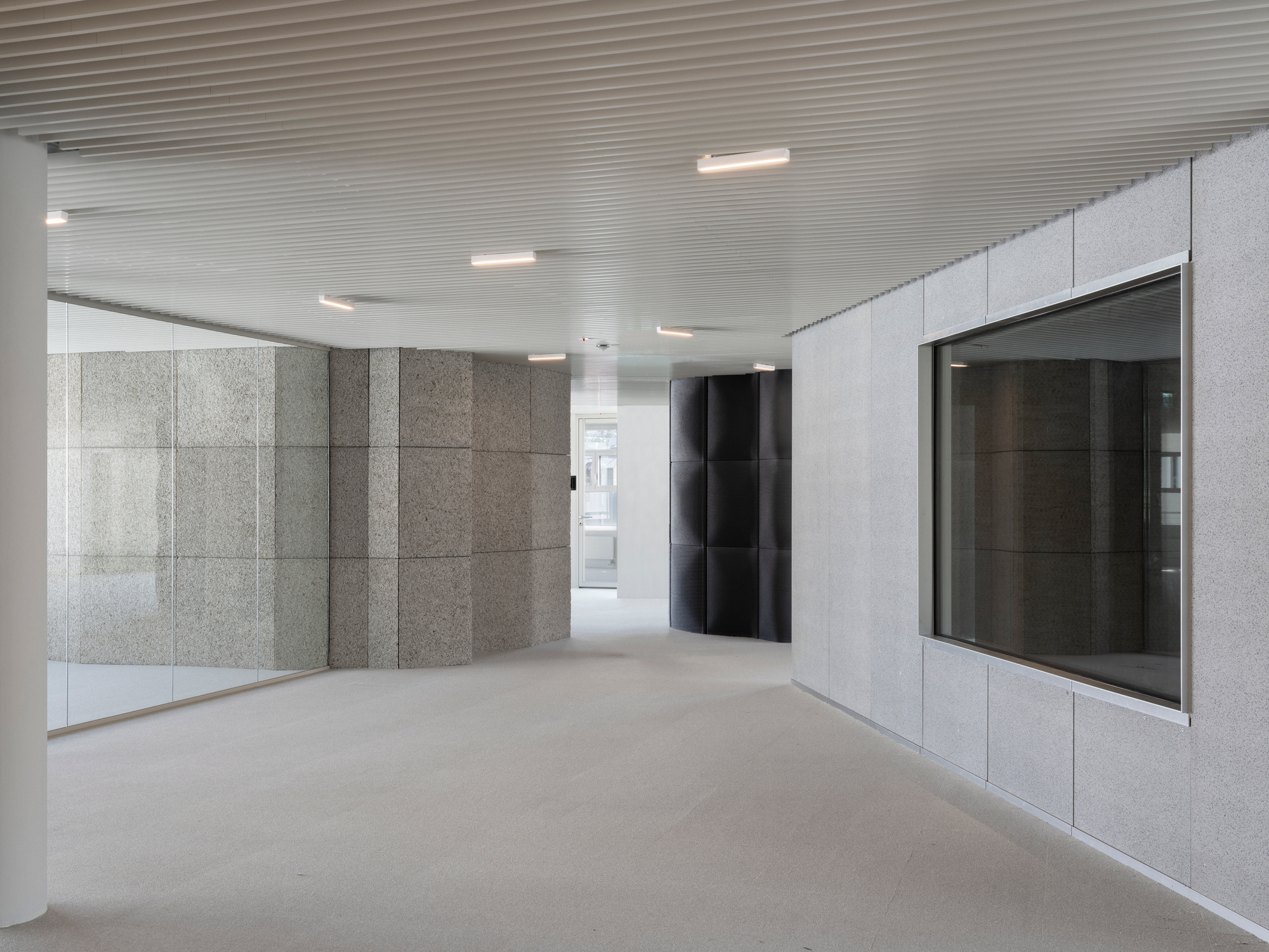 Lobby space with textured grey stone wall panels, black elevator doors, and ribbed metal ceiling with recessed lighting
