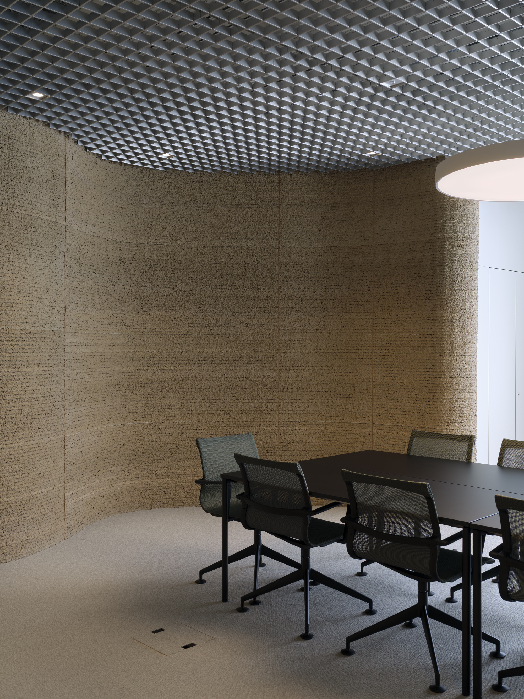 Meeting room with curved textured wall panels and perforated metal ceiling beneath diffused light