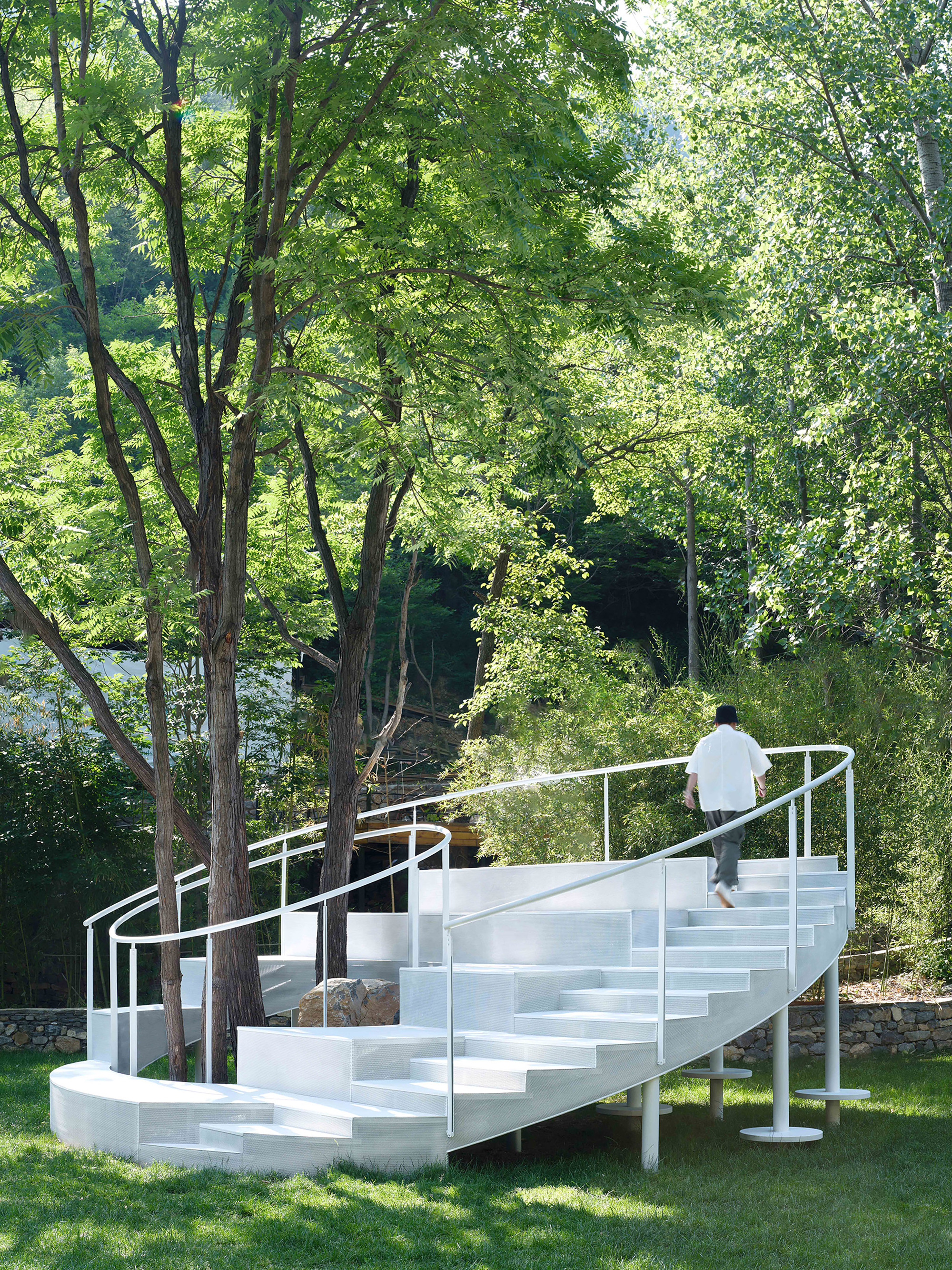 Person ascending the white spiral stair with open risers and tubular steel handrails