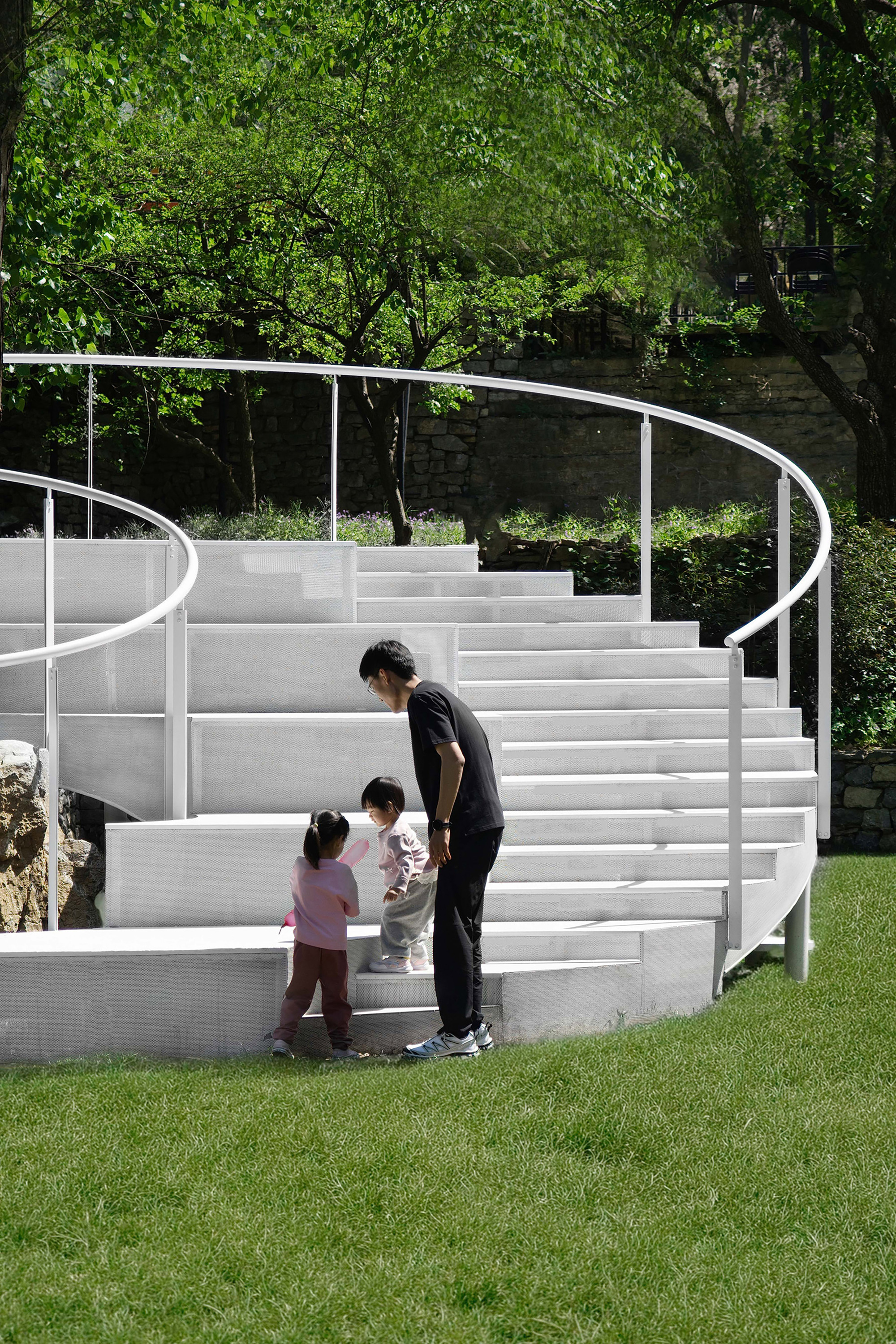 Adult and two children standing on the white curved seating tiers in daylight