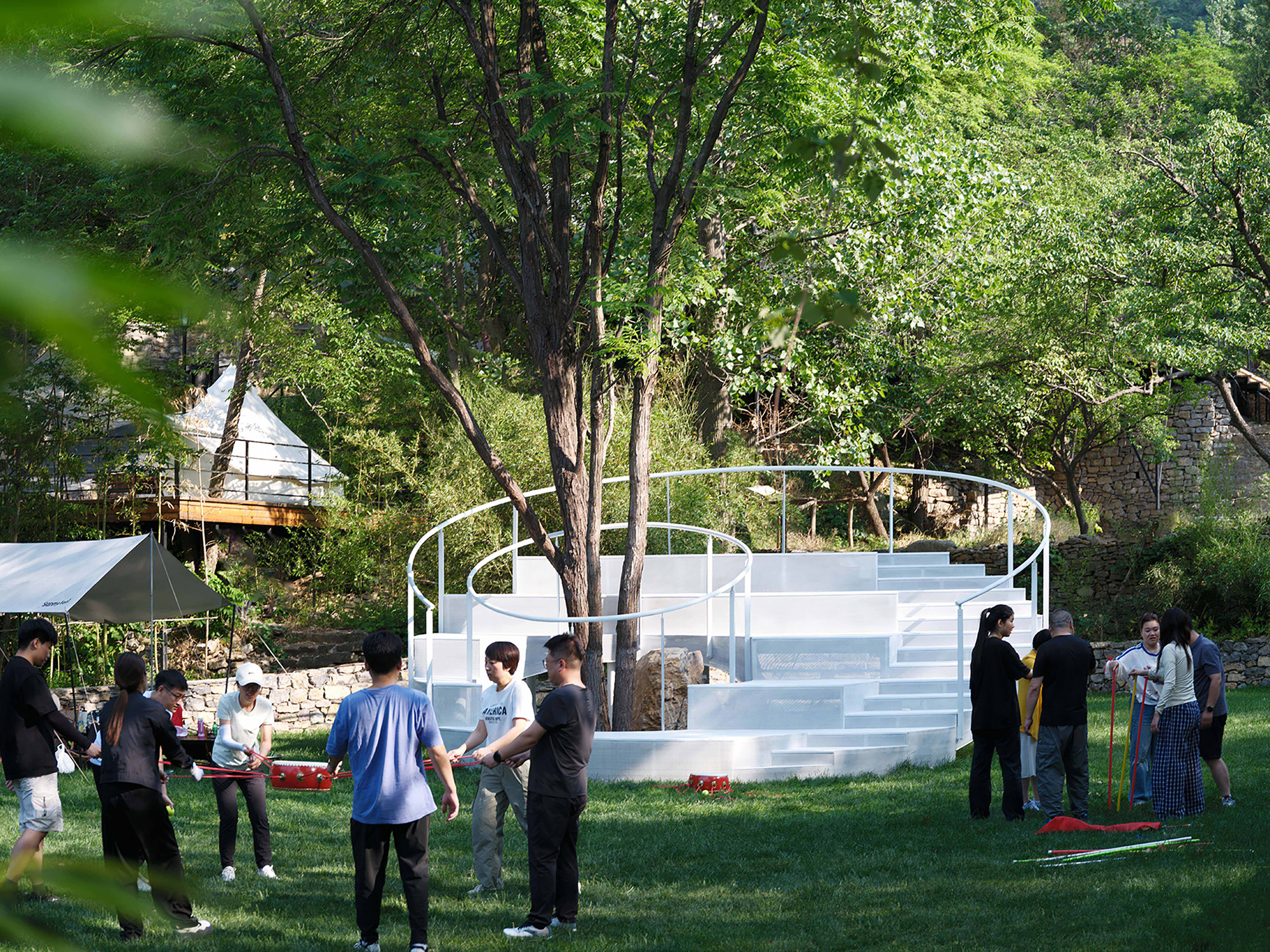 Circular white platform with integrated stairs wrapping around tree trunks under dappled sunlight