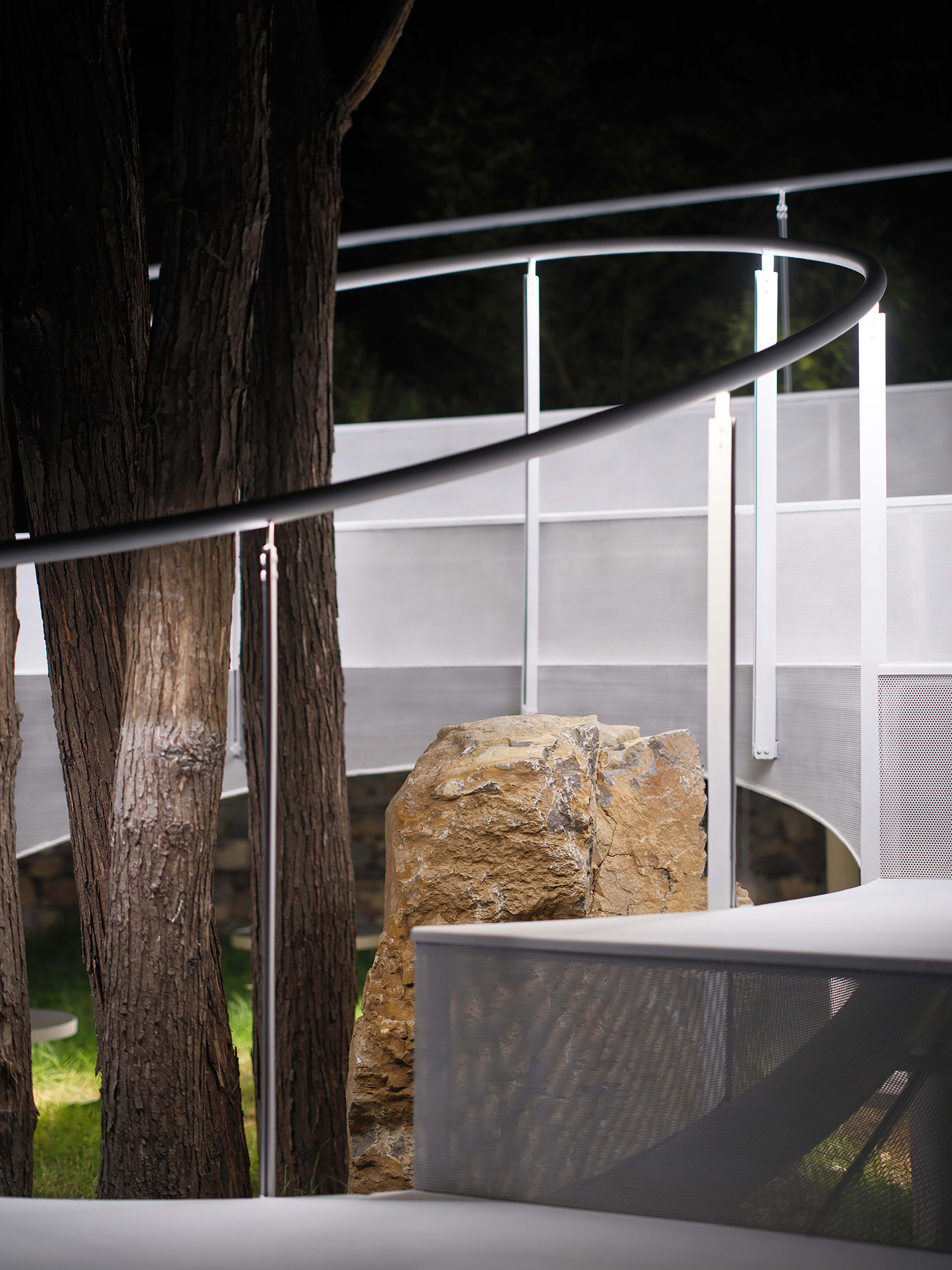 Close-up of tree trunks threading through white railings and mesh panels at night