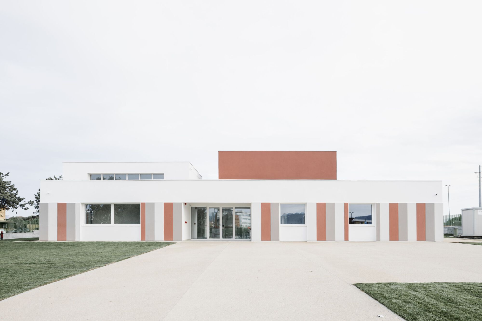 Frontal view of the white facade with terracotta vertical panels and a raised terracotta roof volume