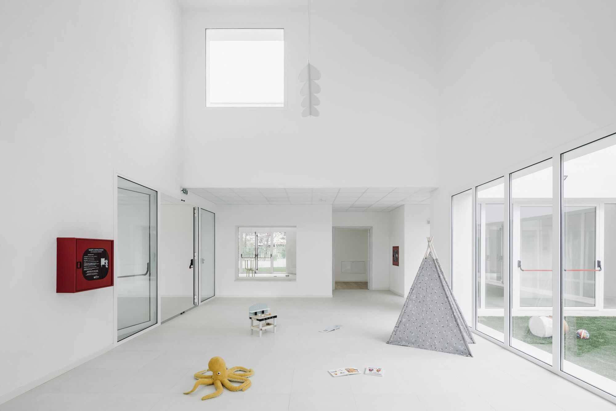 White interior room with floor-to-ceiling glazing, clerestory window, and scattered toys on polished concrete floor