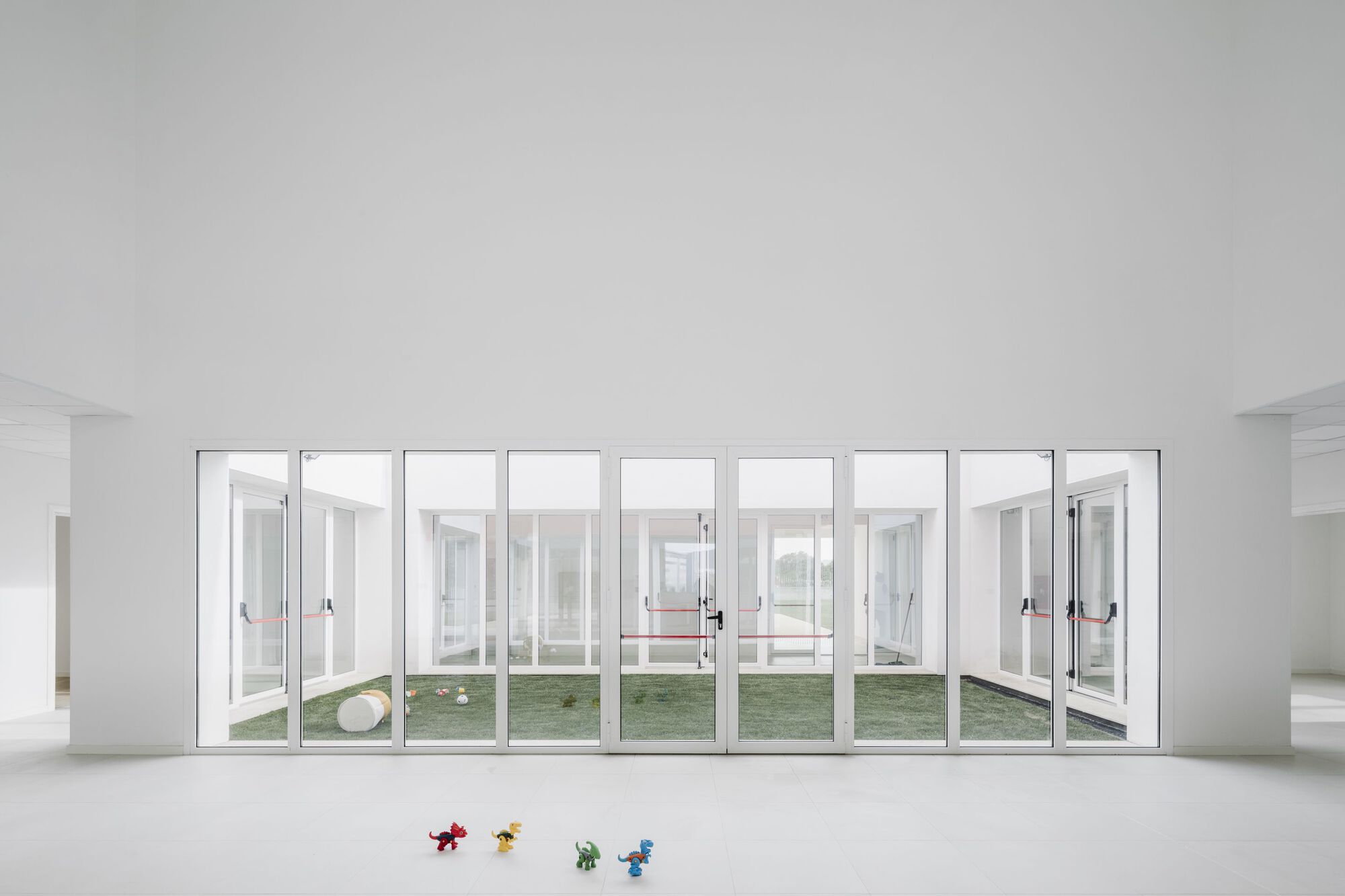 Interior view of nine-panel glazed wall opening to a courtyard with scattered plastic toys