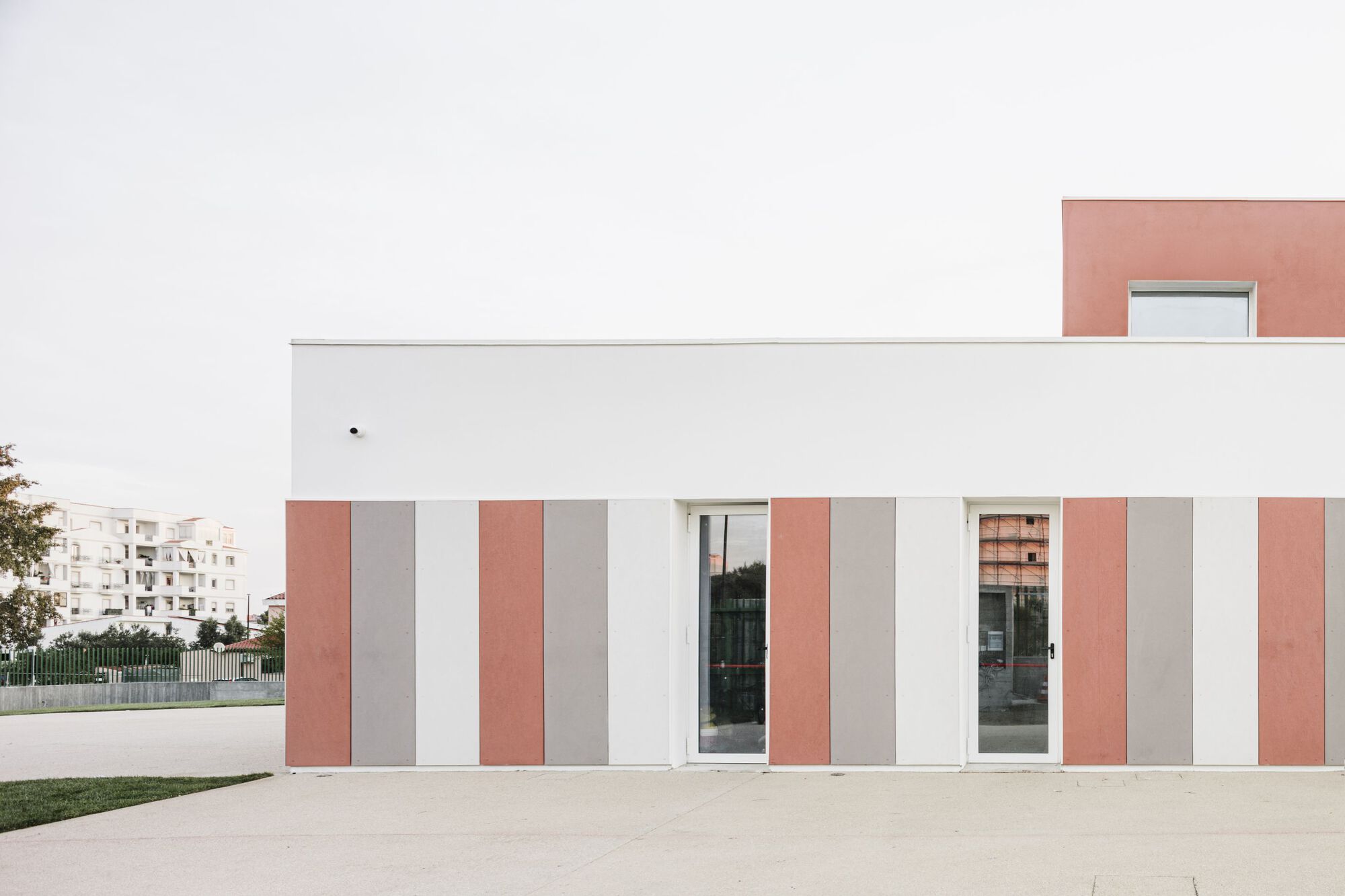 Entrance facade with alternating vertical bands of terracotta, grey and white panels framing glazed doors