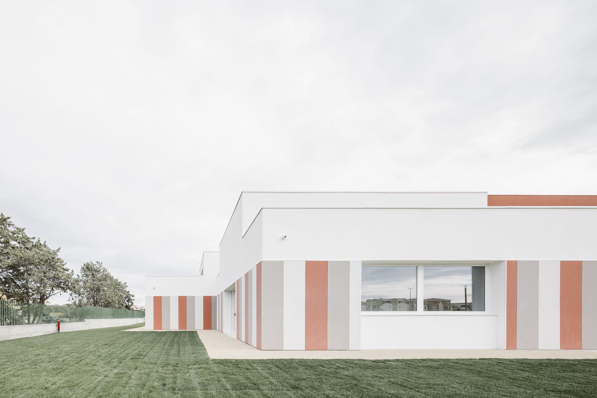 Side elevation showing the striped facade extending along a covered walkway beside a mown lawn