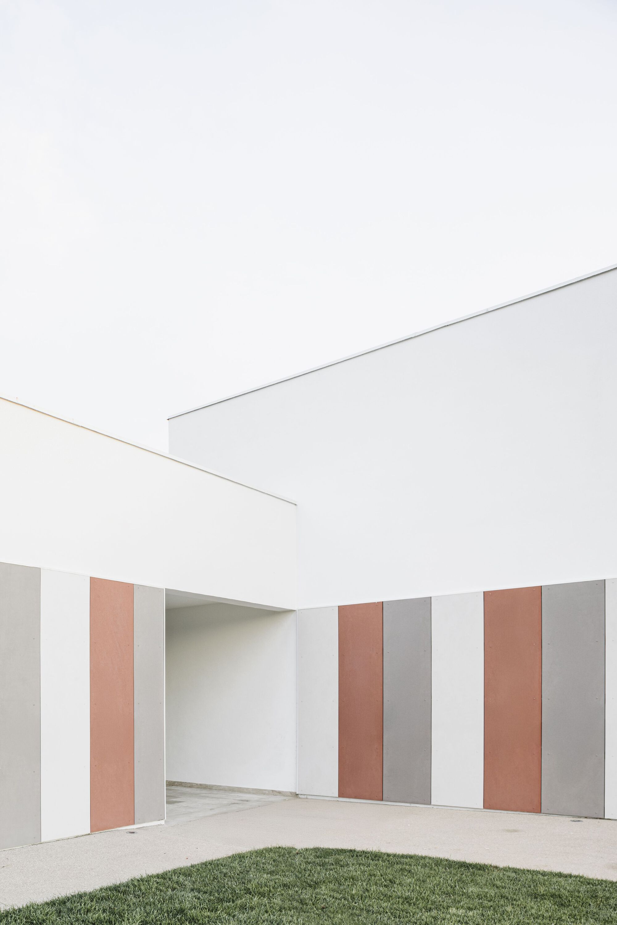Covered passage with vertically striped wall panels in terracotta, grey and white beside the lawn